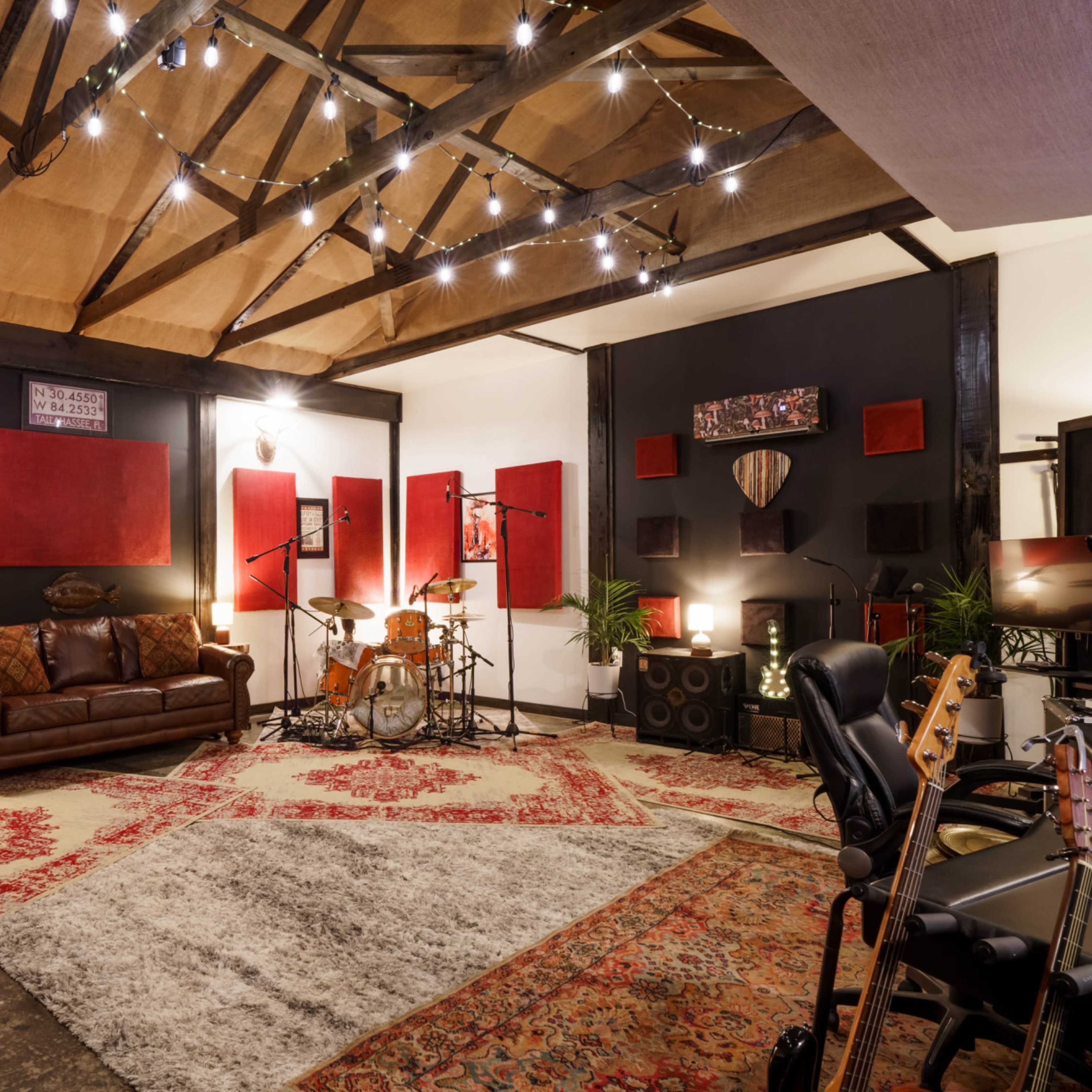 A music studio with a drum set, guitars, and soundproofing panels, featuring a rustic ceiling and warm lighting.