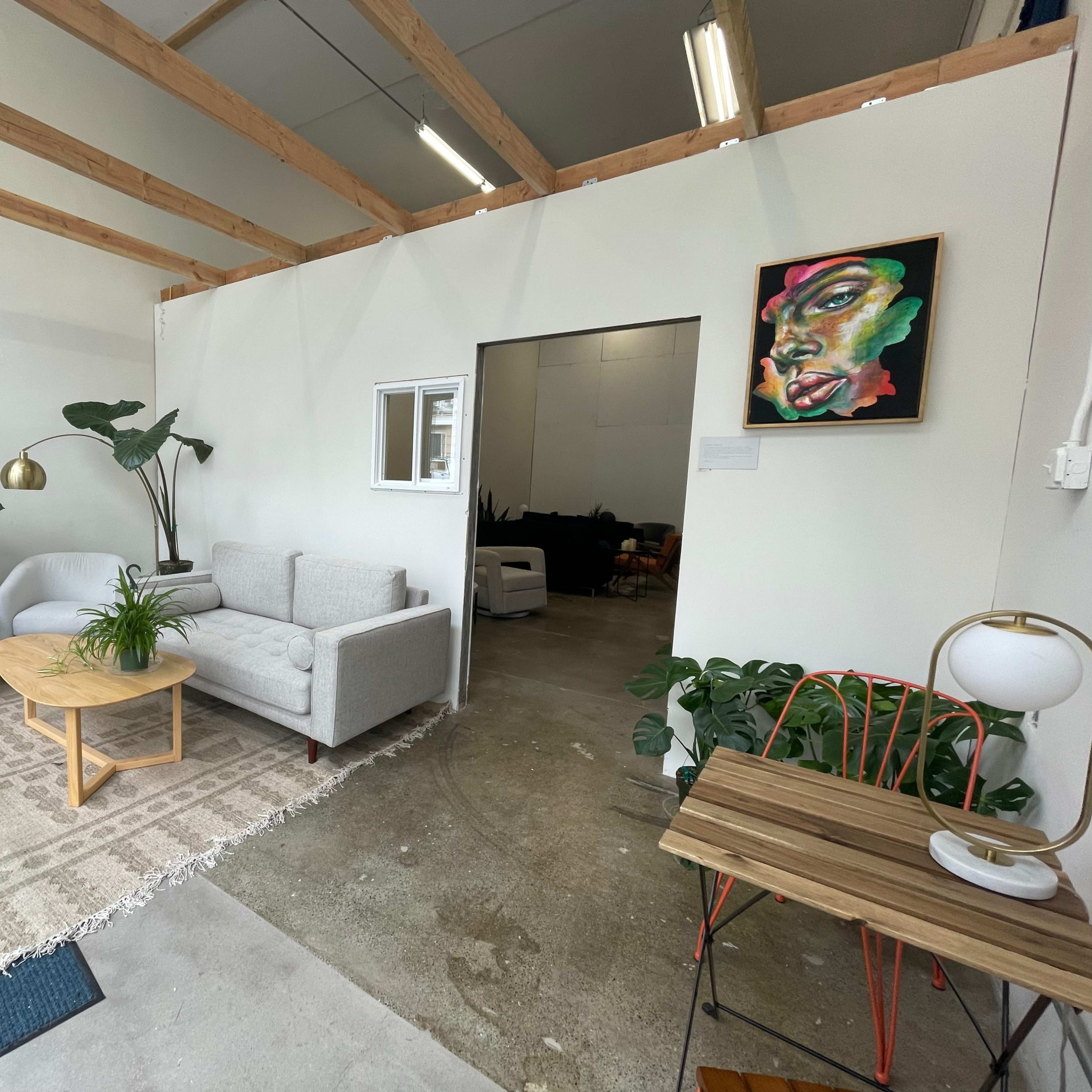 A modern, minimalistic interior space with a seating area that includes a light gray sofa, two white armchairs, a round wooden table, and decorative plants.
