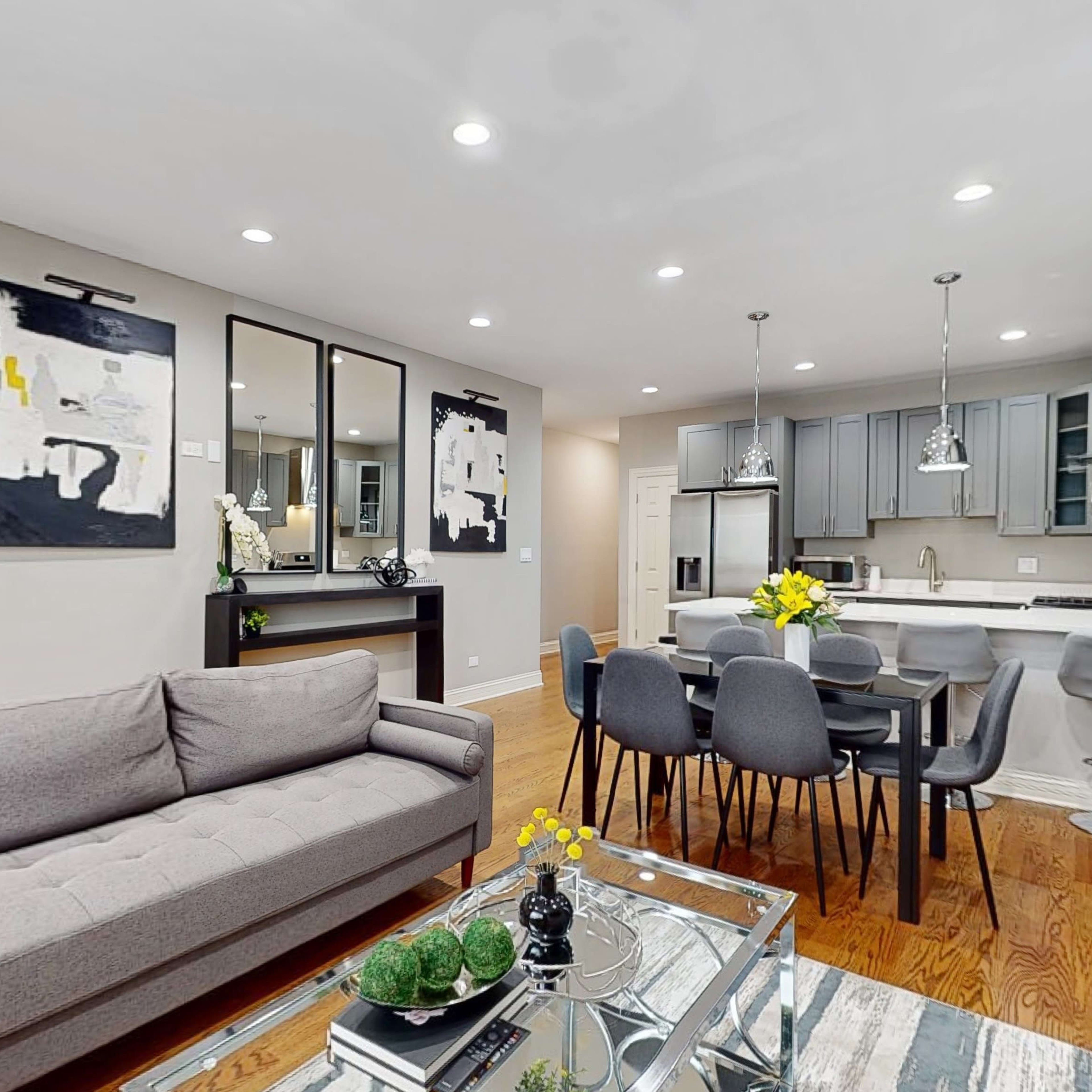 A modern living and dining area with a gray sofa, a dining table surrounded by gray chairs, and a kitchen area in the background.