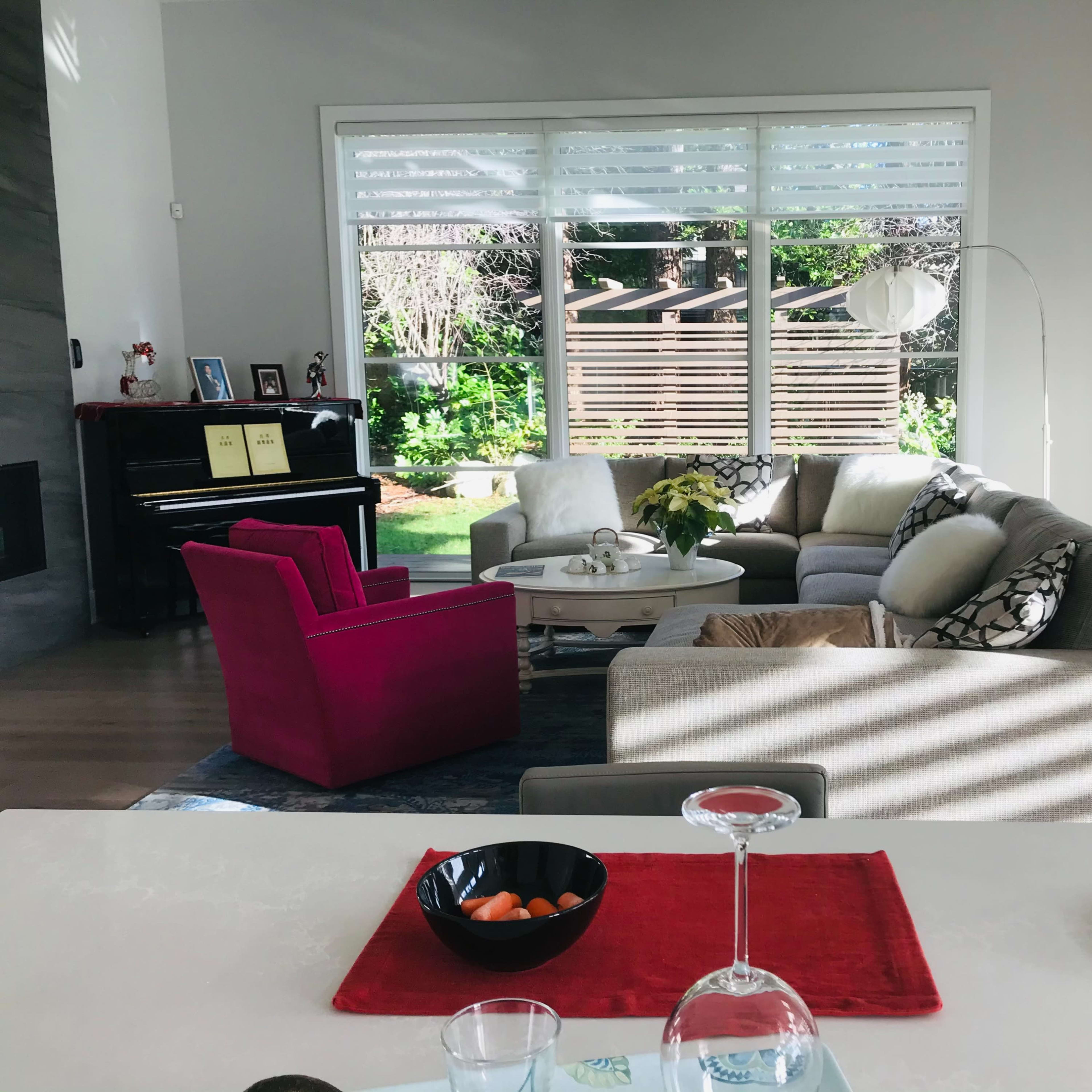 A modern living room with a mix of gray and pink furniture, large windows, and a view of a garden outside.