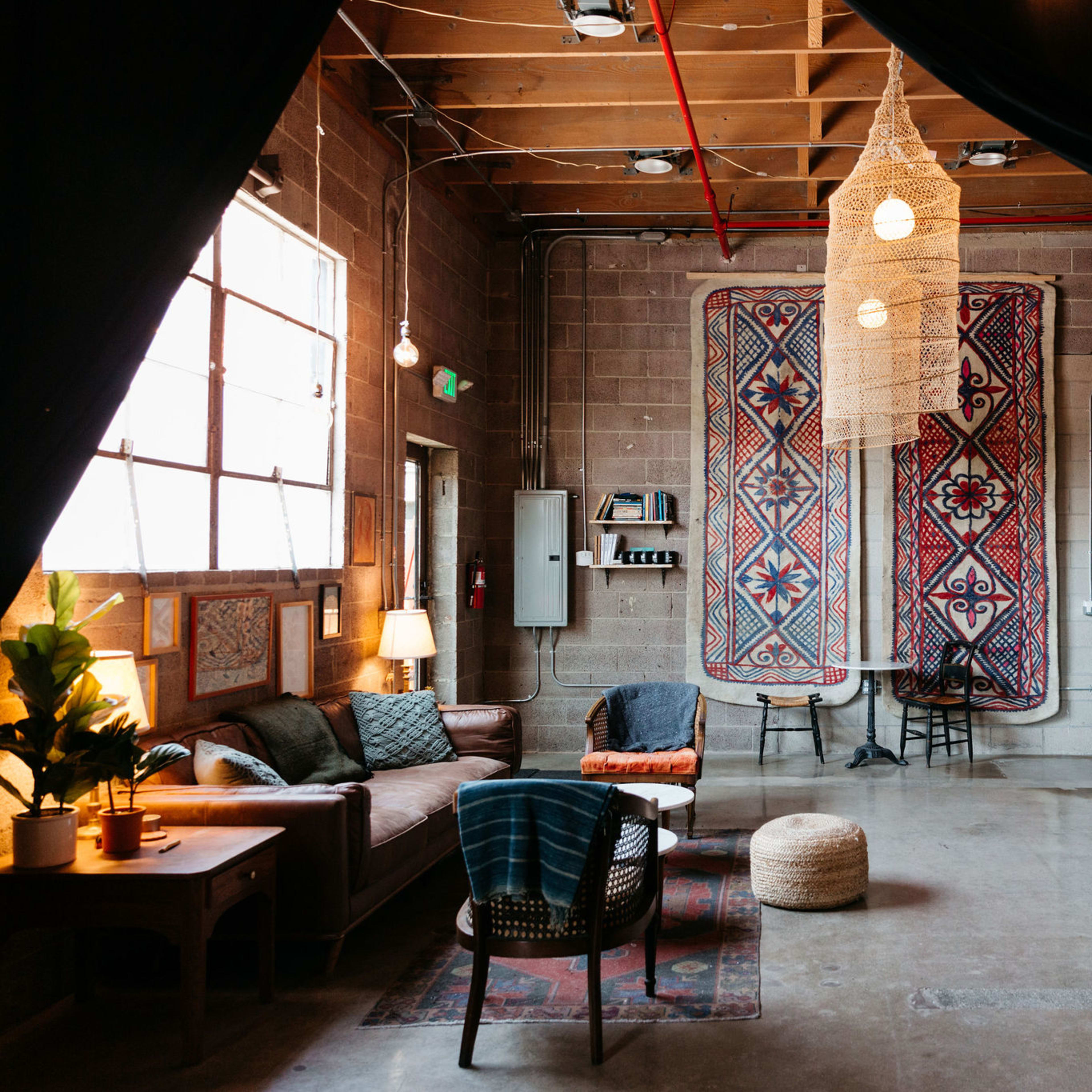A cozy sitting area with a patterned rug, various seating options, and decorative wall hangings in an industrial-style room.