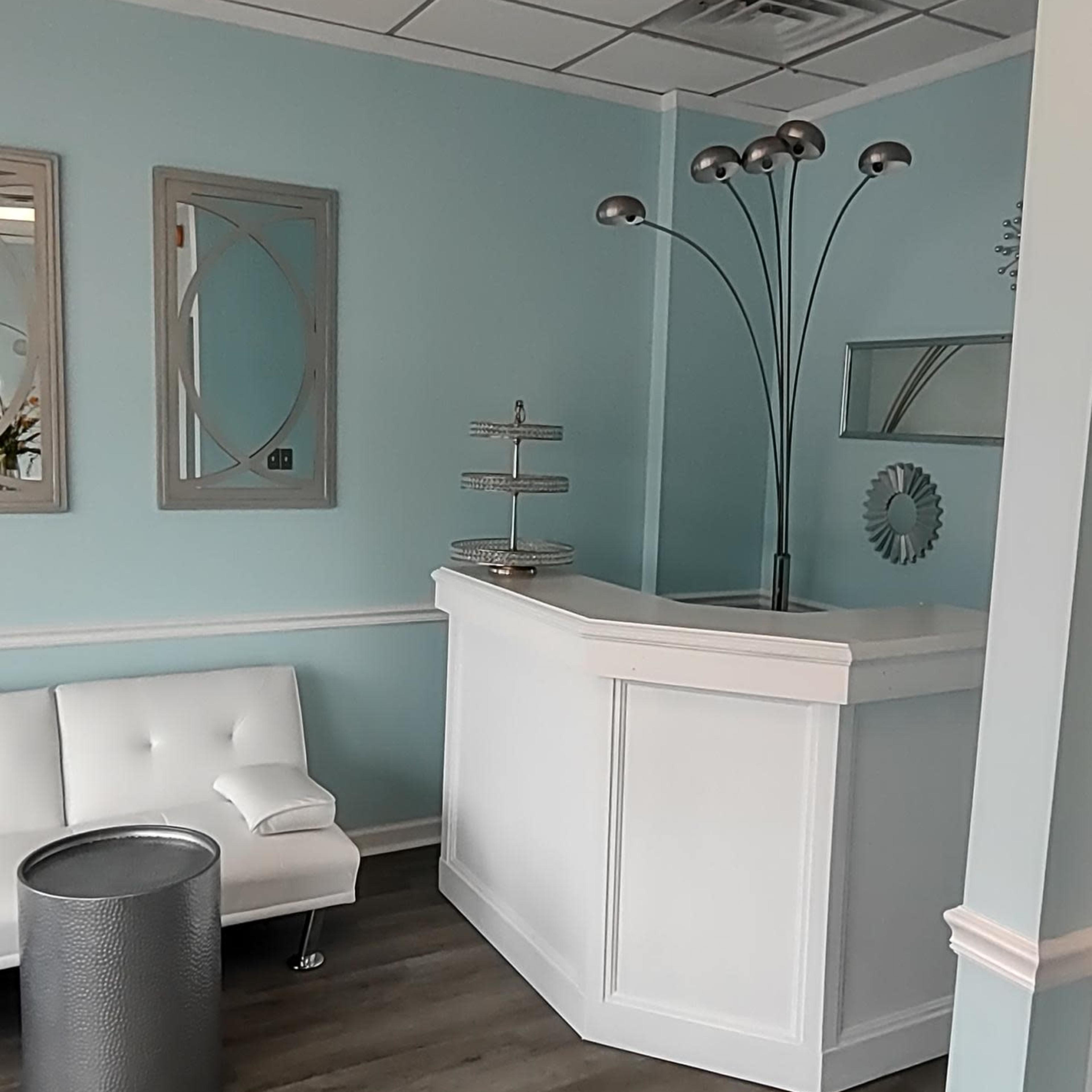 A reception area with a white counter, a light blue wall, a gray round table, and modern lighting fixtures.