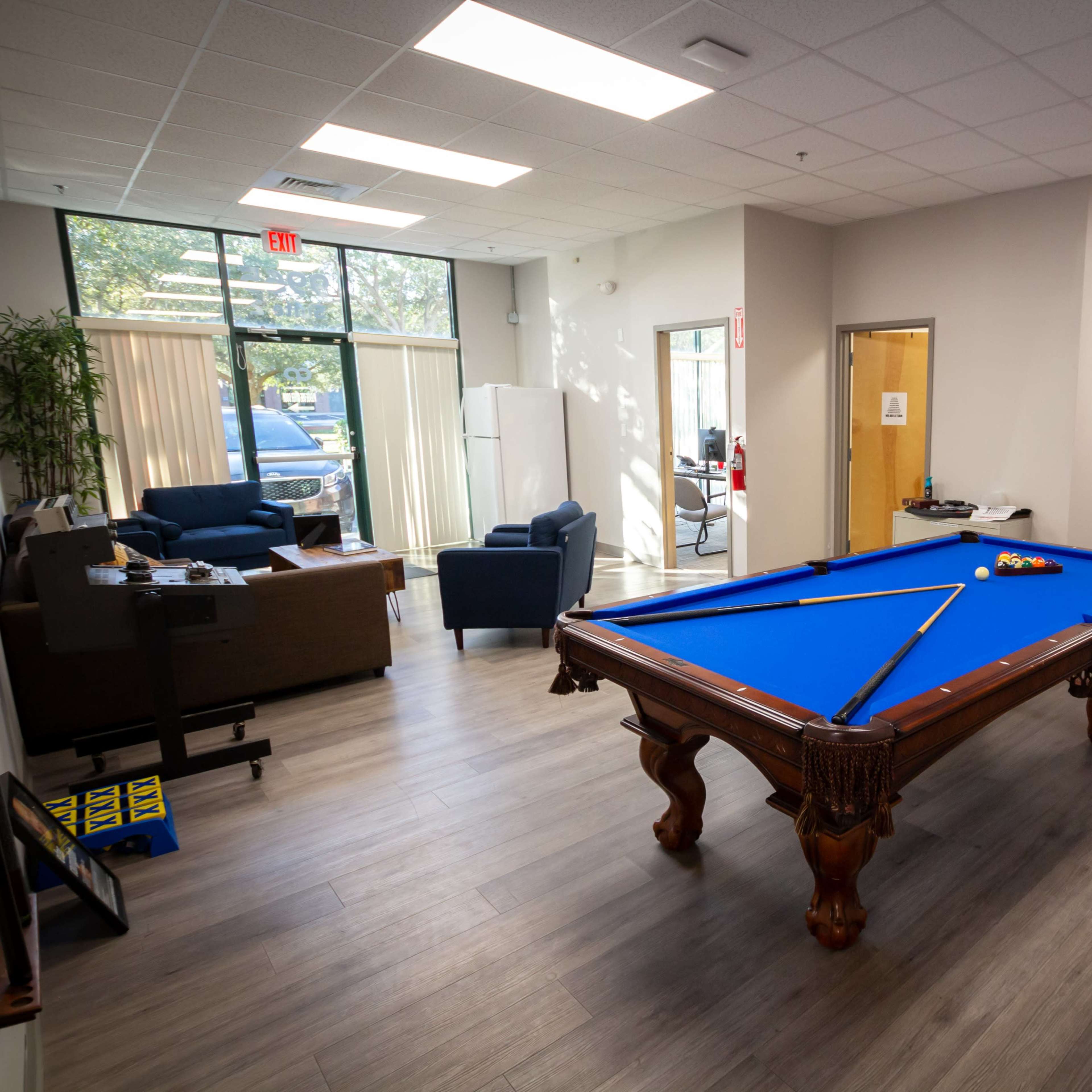 A game room featuring a blue pool table, a foosball table, and seating areas with a couch and water cooler.