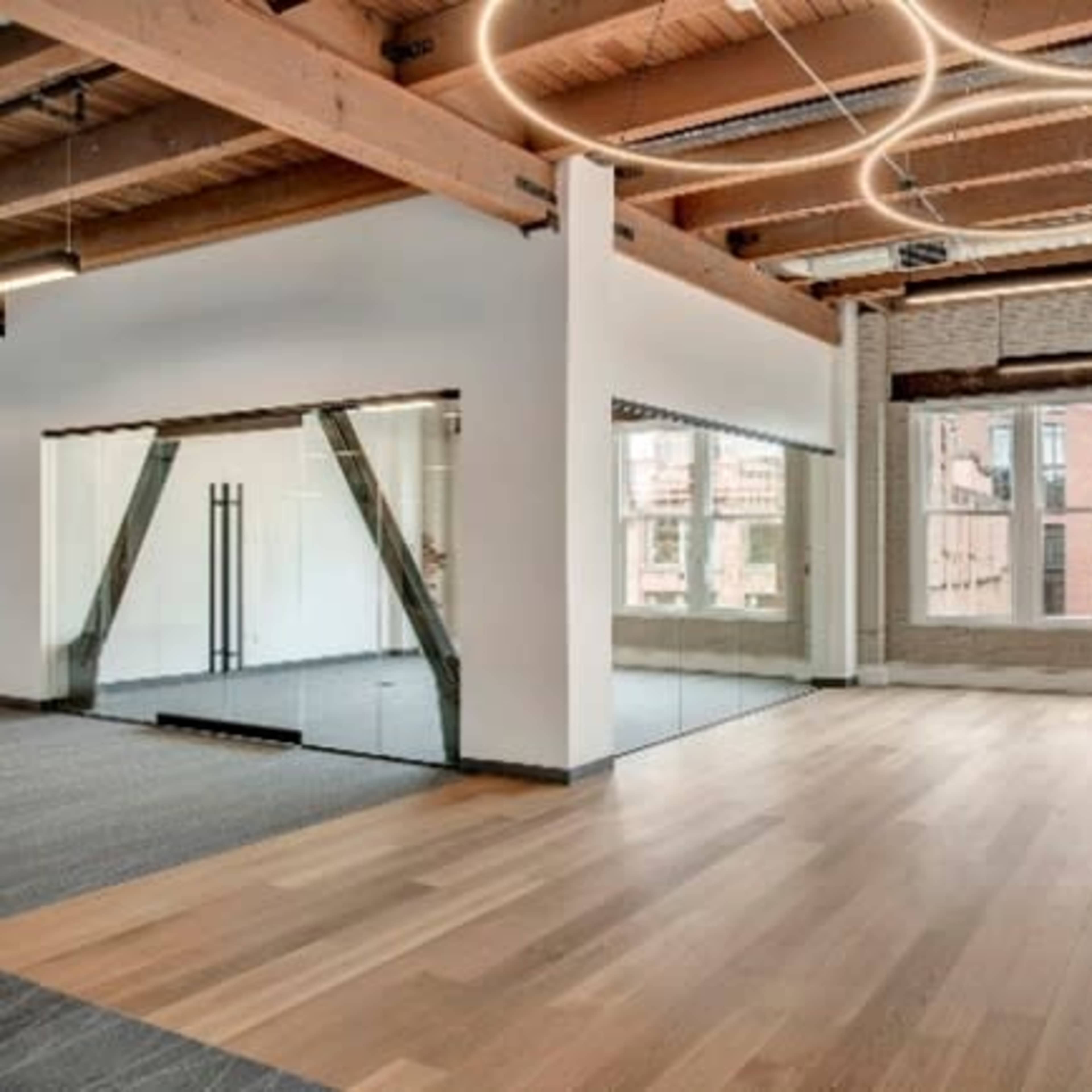 A spacious, modern room with wooden flooring, exposed beams, and large windows.