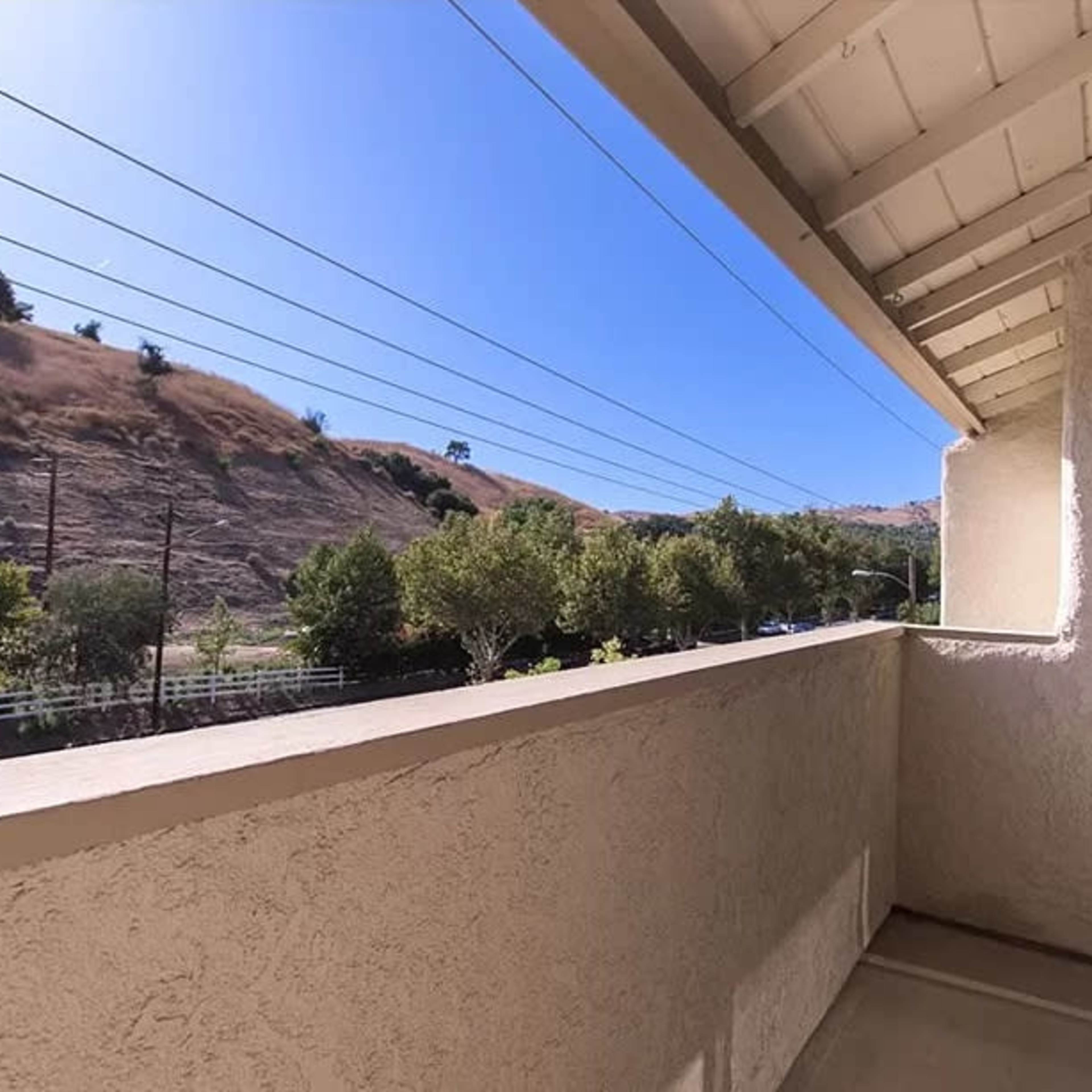 A balcony with a view of a hillside and power lines under a clear blue sky.