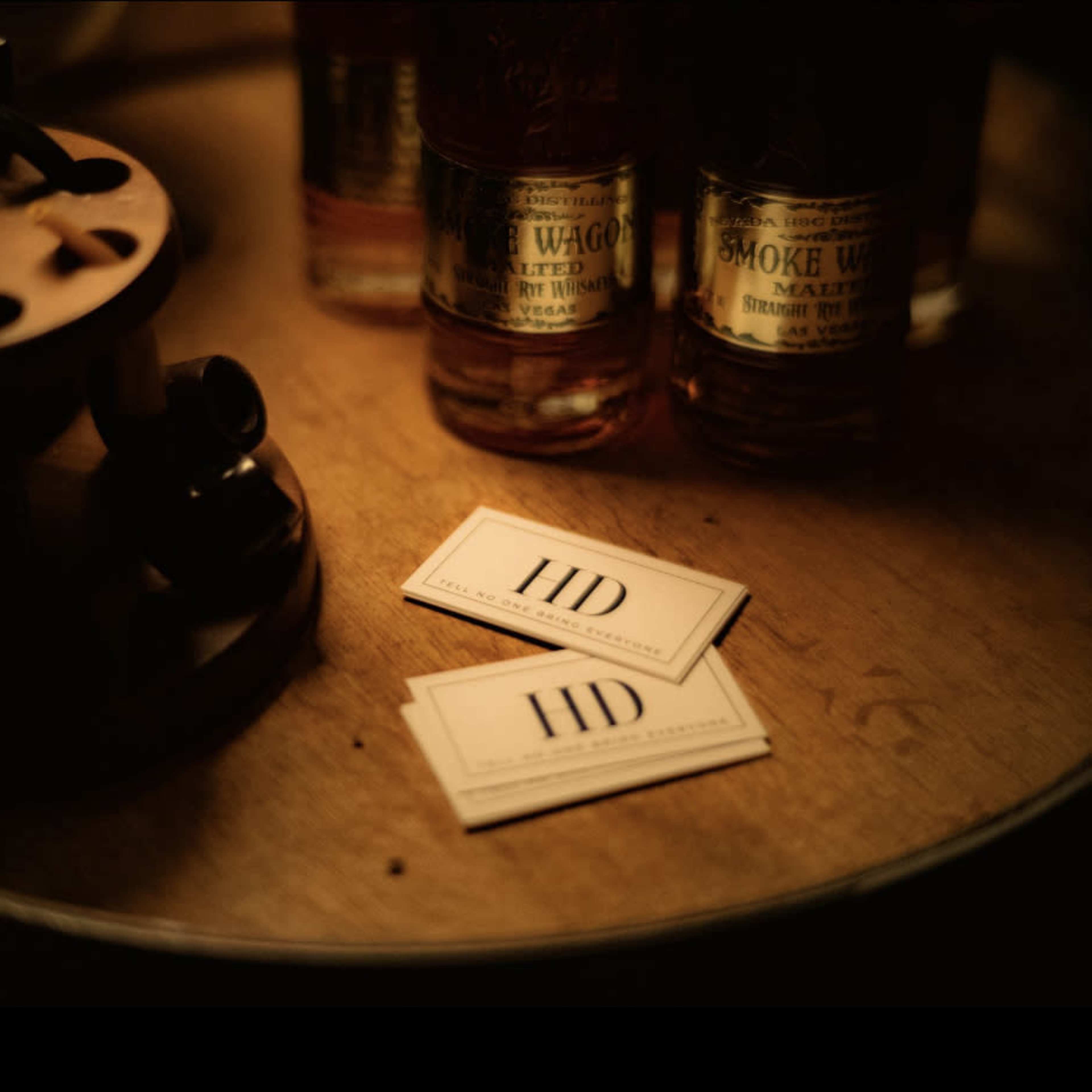 A wooden table features two cards labeled "HD" next to bottles of whiskey.
