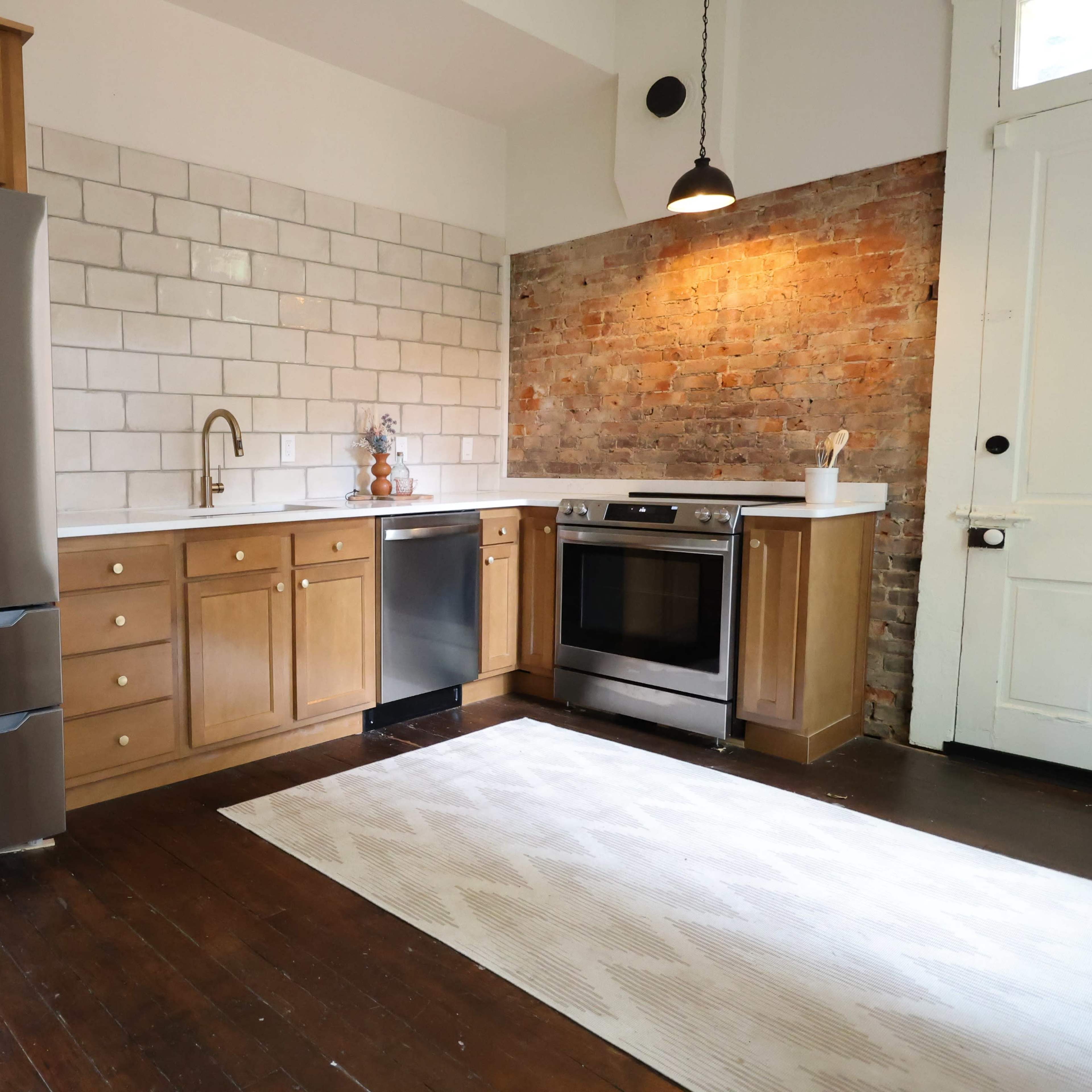 A modern kitchen featuring stainless steel appliances, wooden cabinetry, and exposed brick walls.