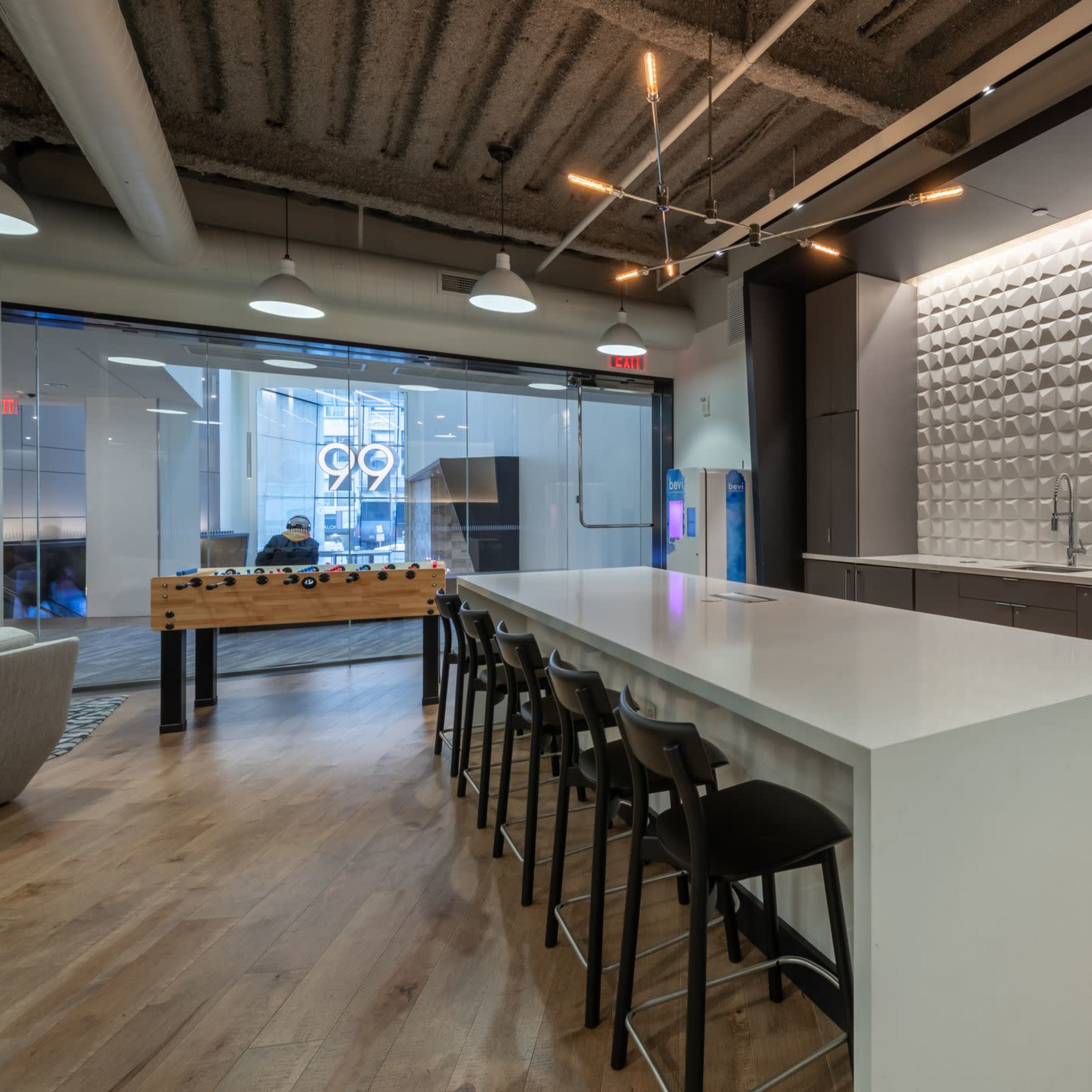 A modern kitchen space featuring a large white island, a textured backsplash, metal cabinets, and floor-to-ceiling windows.