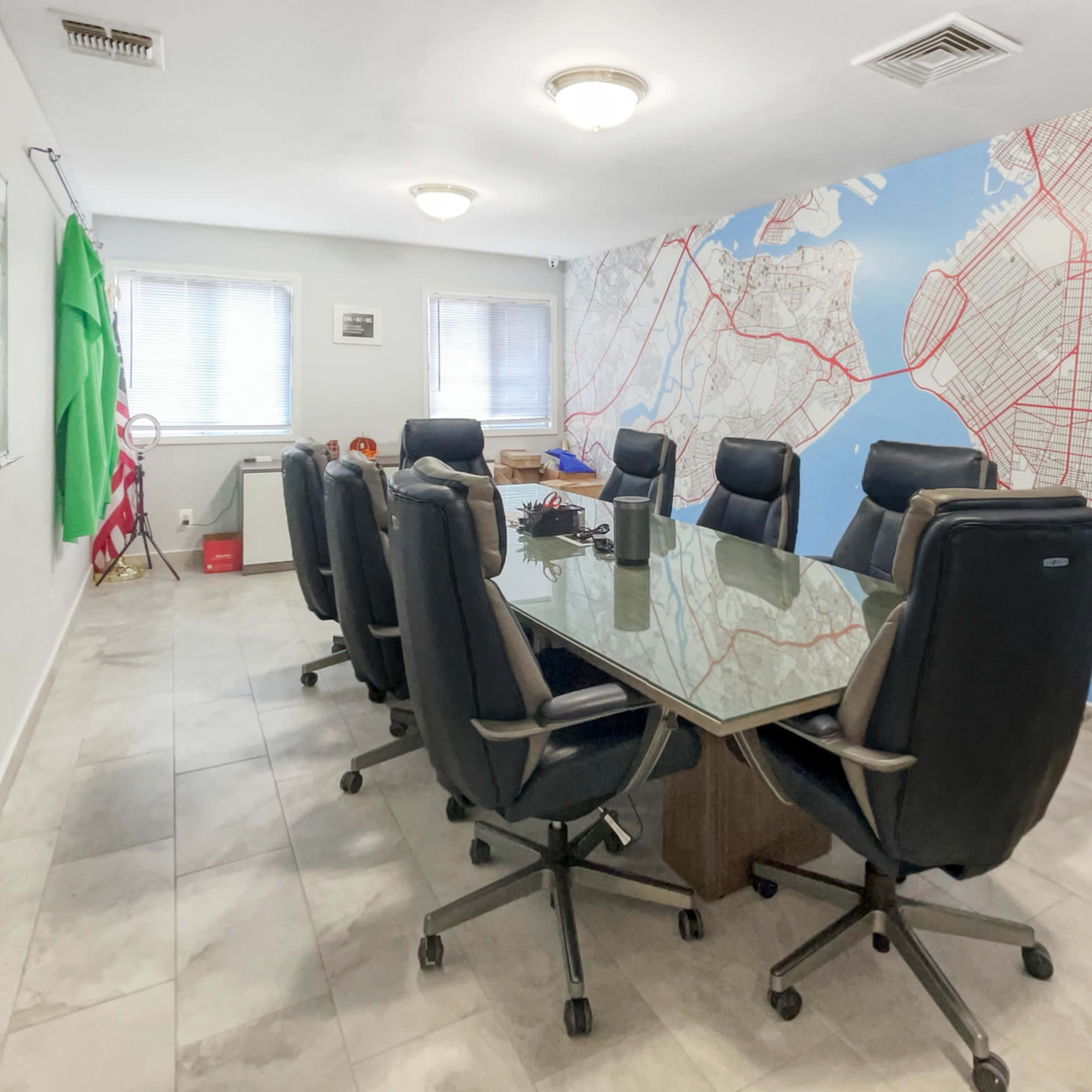 A conference room with a large glass table surrounded by black office chairs, set against a wall featuring a map design.