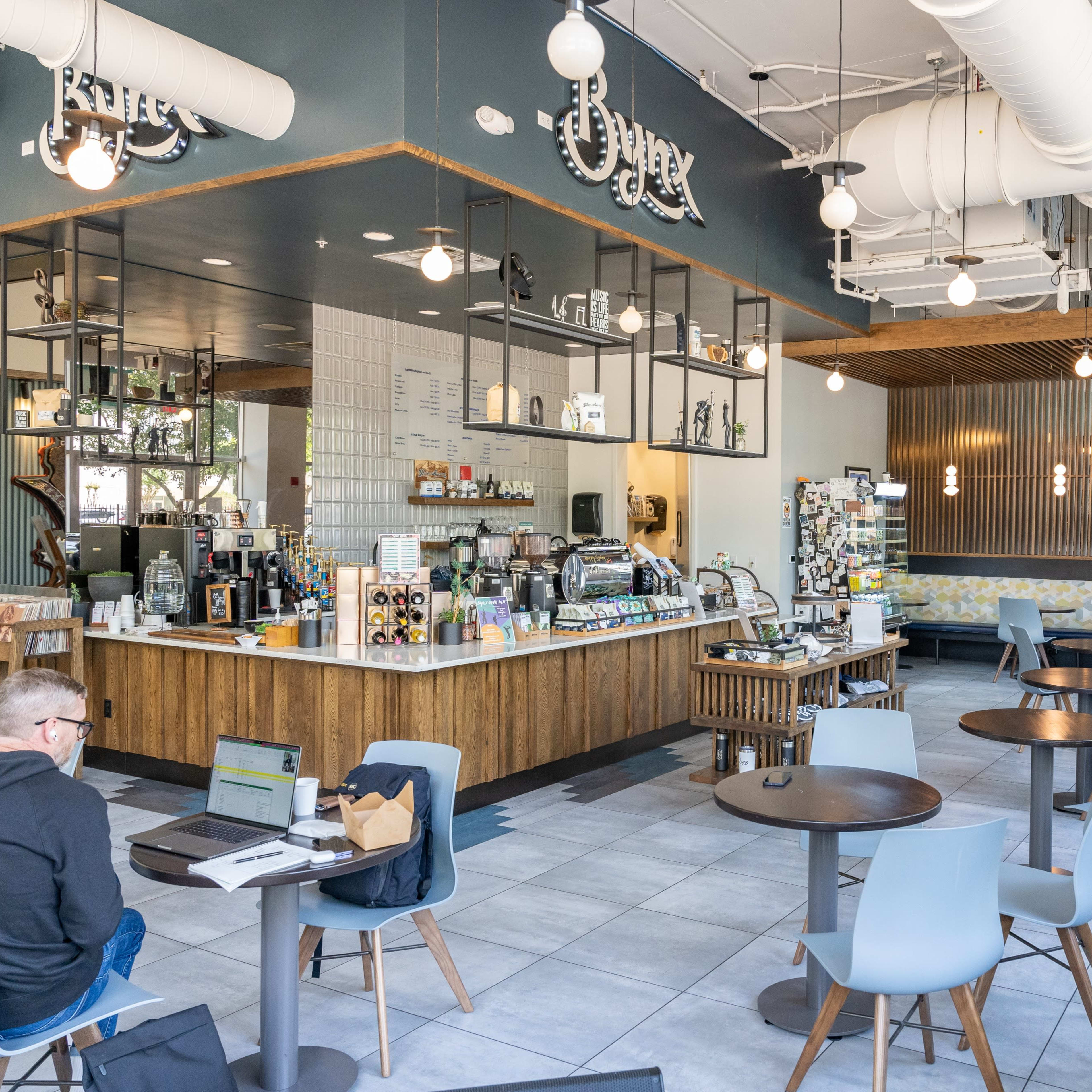 A modern café interior with a counter displaying various drinks and snacks, surrounded by tables and chairs for customers.