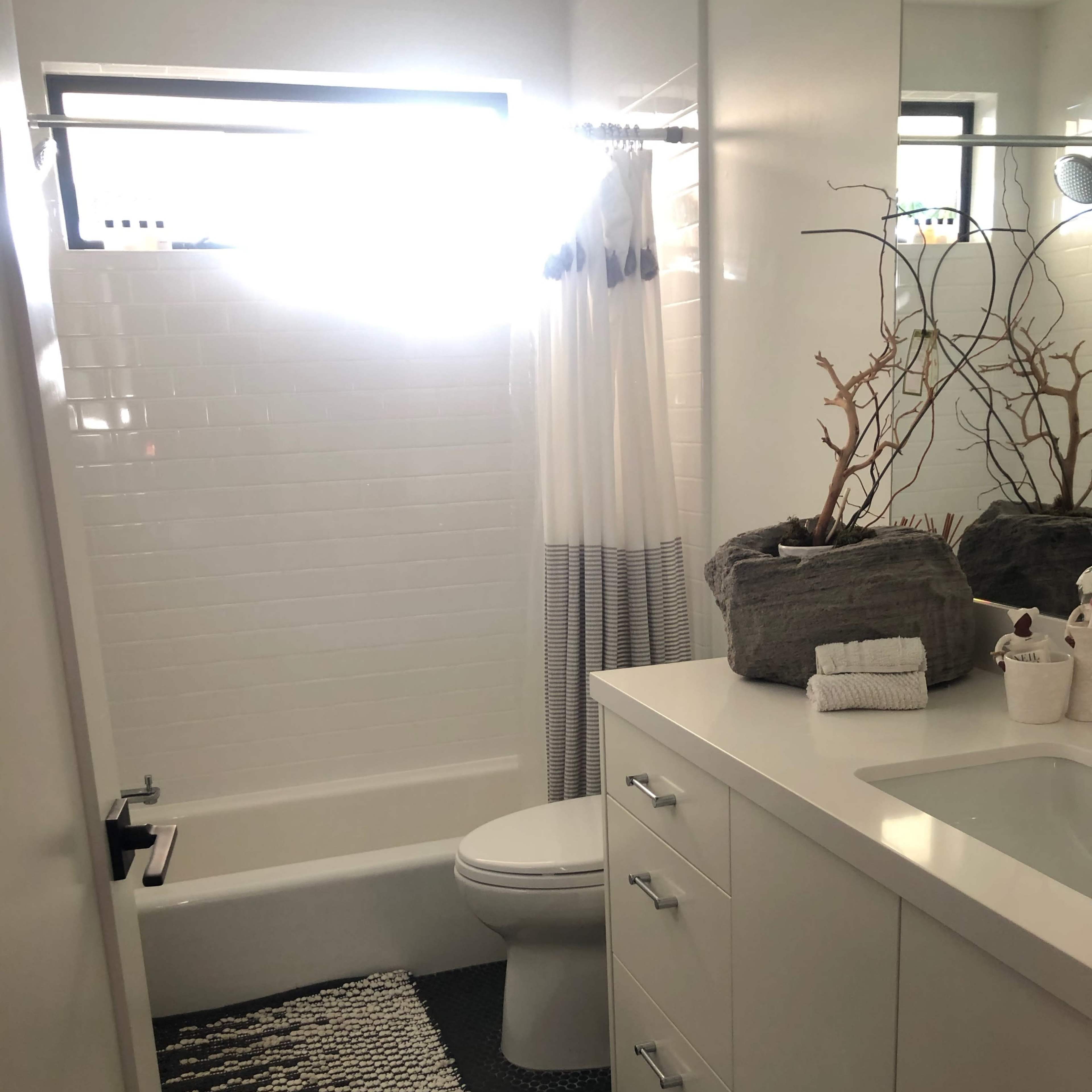 A modern bathroom with a white bathtub, a countertop with a sink, a large mirror, and a textured rug on the floor.