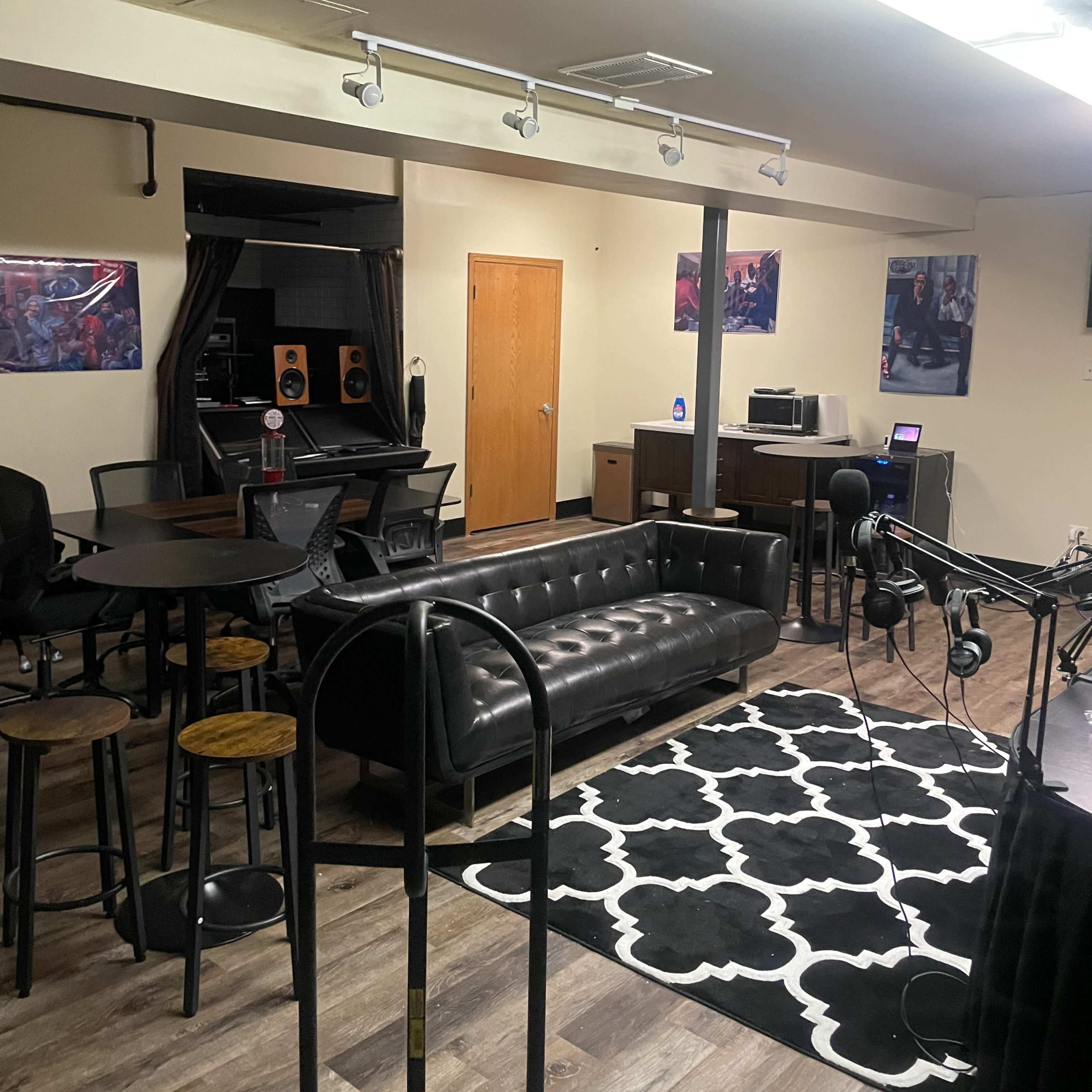 A music studio with a black leather couch, a dining table with stools, and recording equipment in the background.
