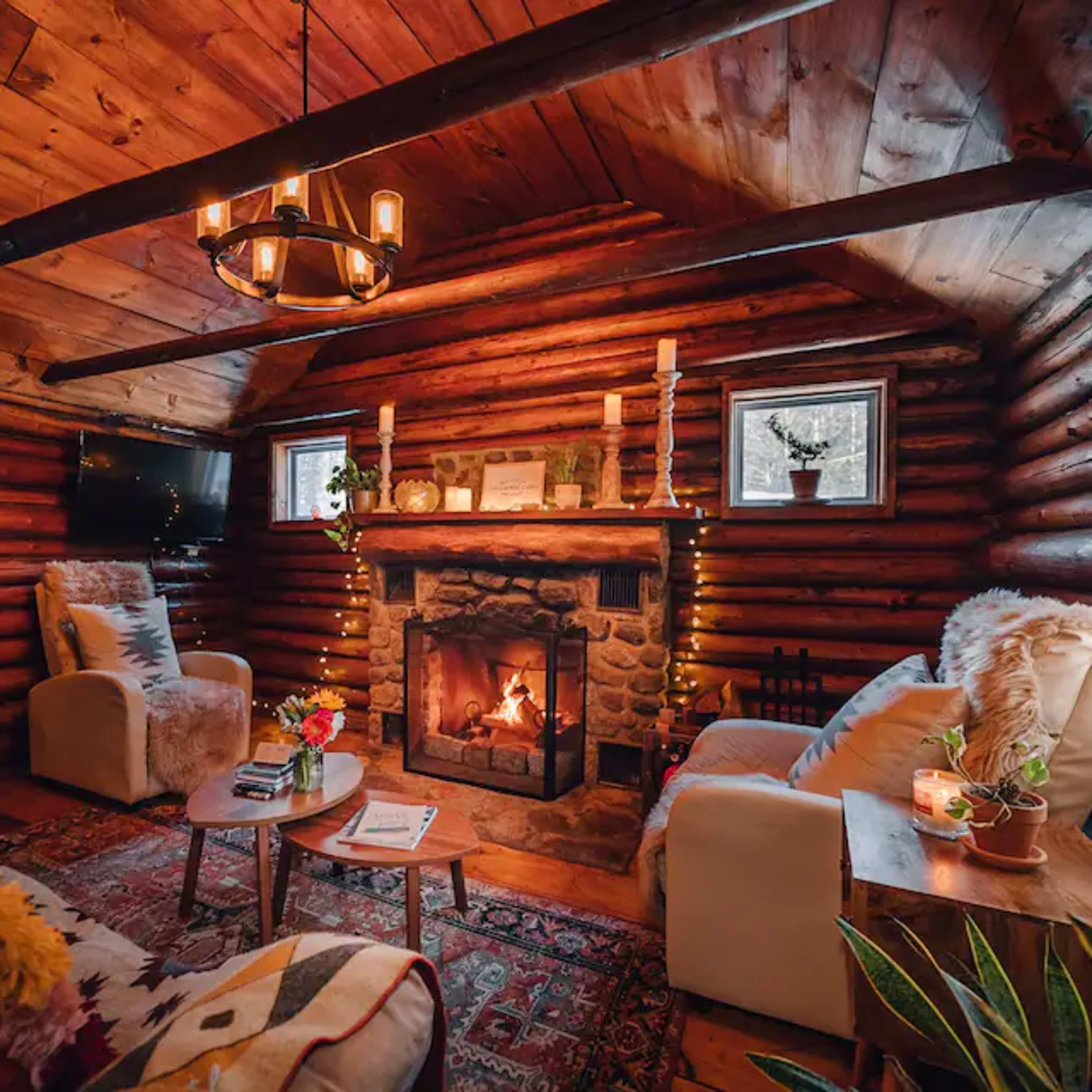 A cozy log cabin interior with a stone fireplace, two armchairs, and a wooden ceiling.
