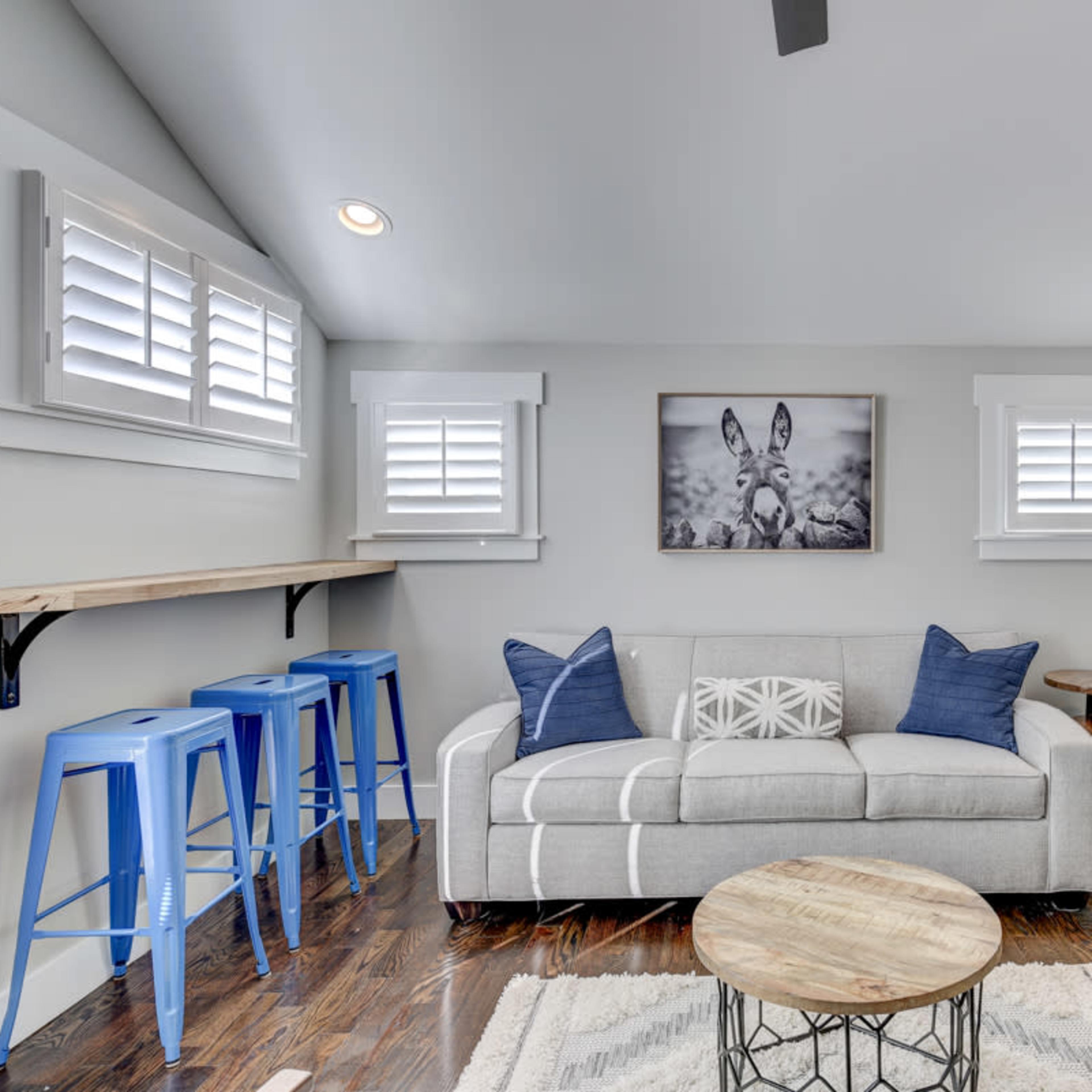 A modern living room with a gray sofa, blue bar stools, a wooden coffee table, and a wall-mounted television.