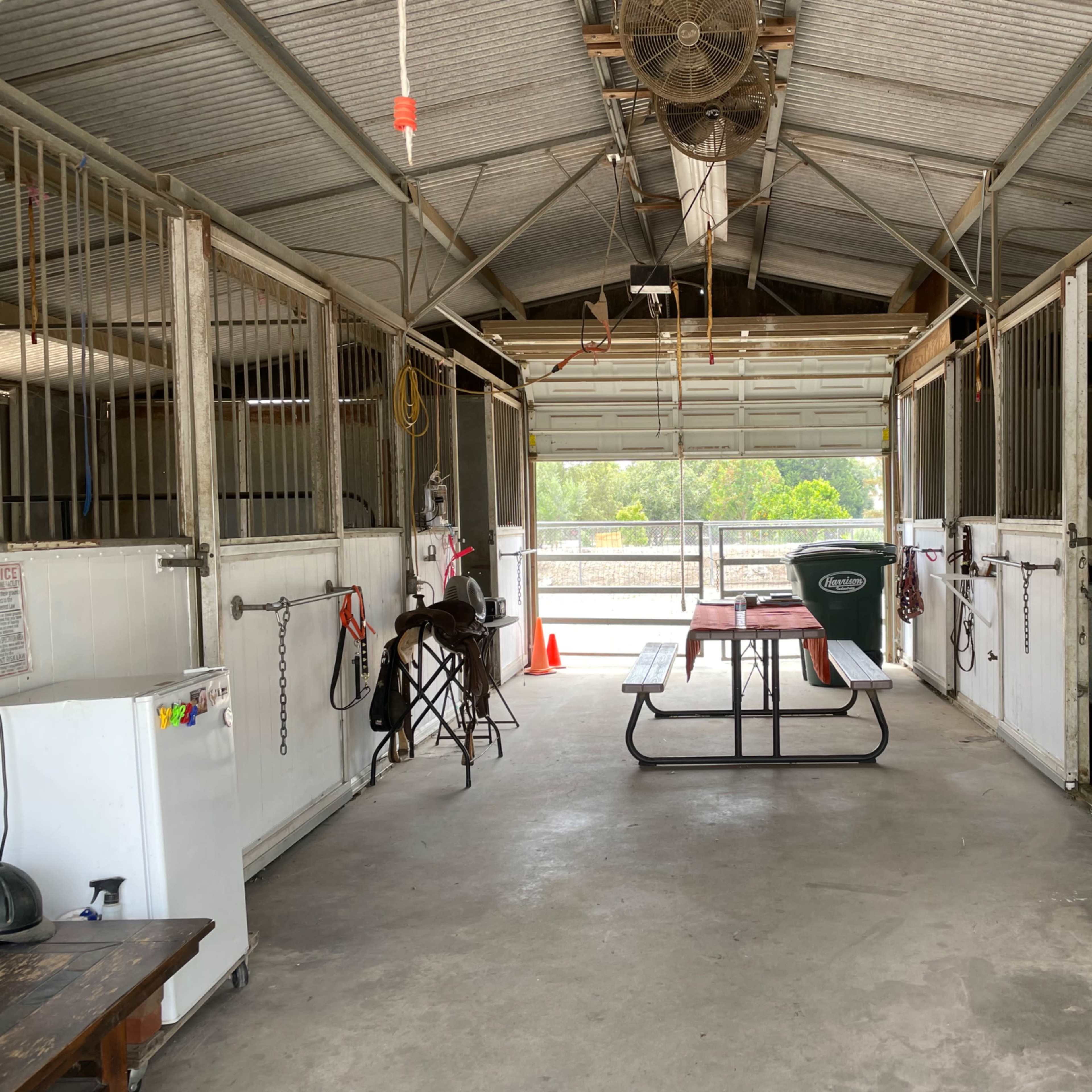 The interior of a horse barn with stalls on either side and a central picnic table.