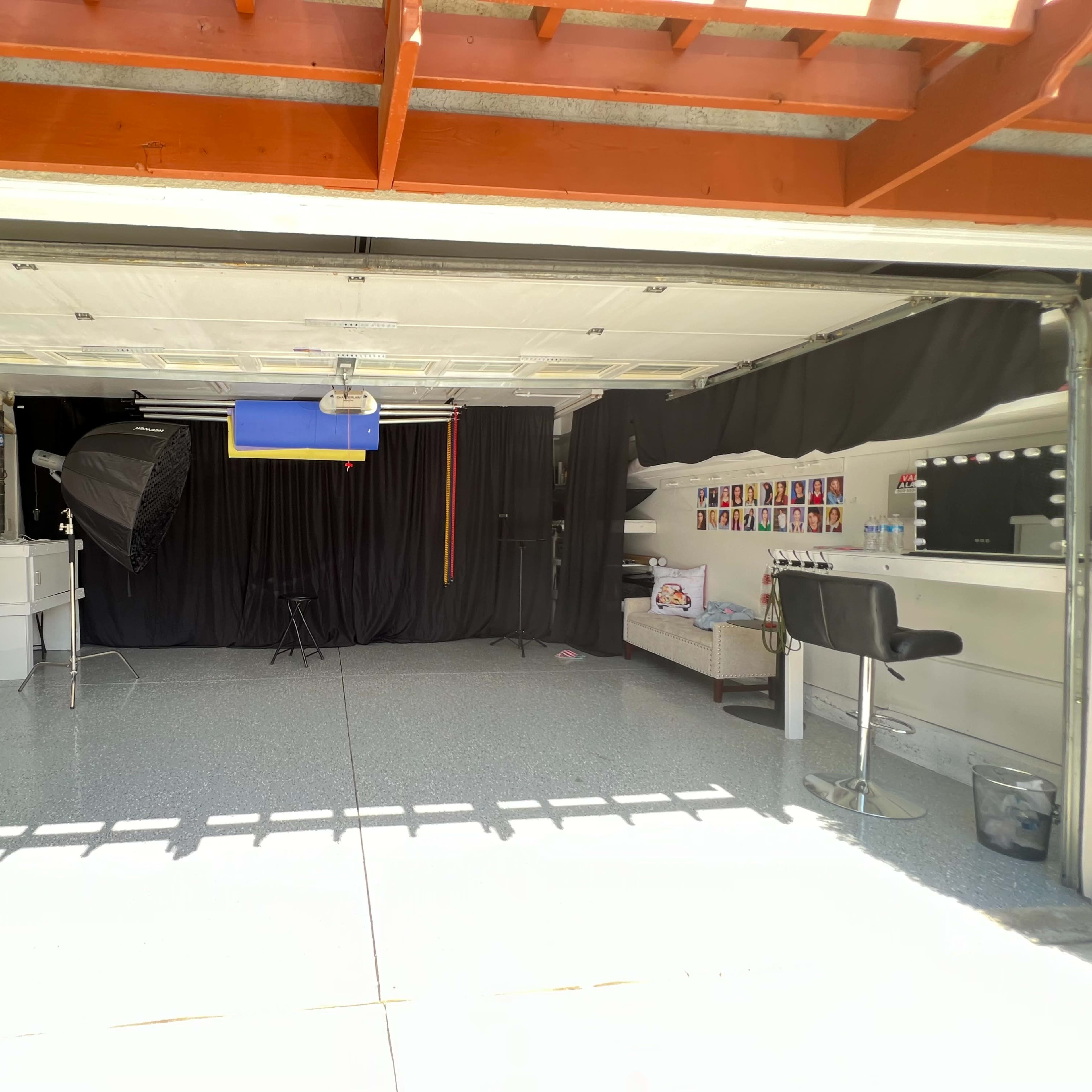 A garage is converted into a photography studio with a black backdrop, lighting equipment, and a seating area.