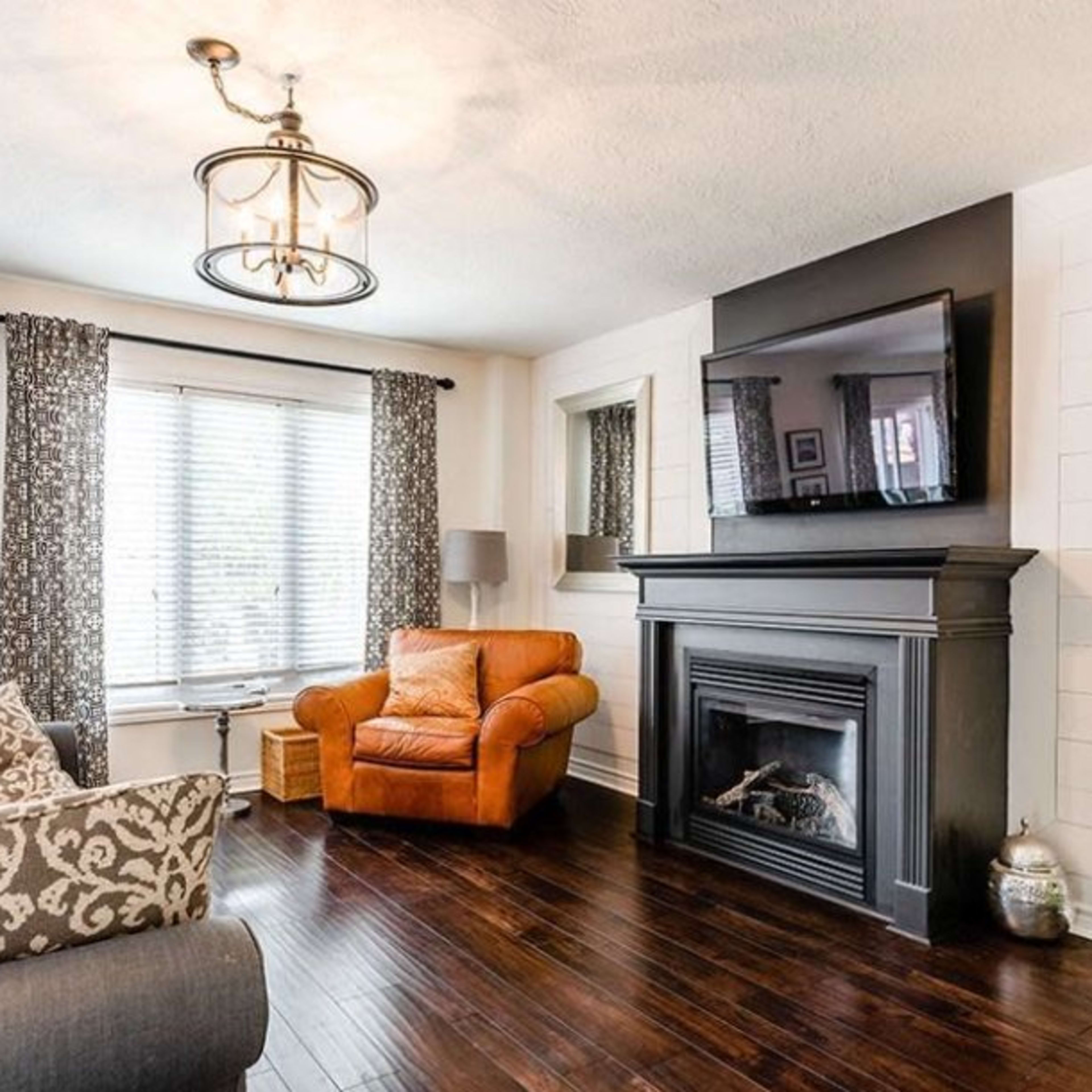 A cozy living room with a brown leather armchair, a black fireplace, a television mounted on a wall, and hardwood floors.