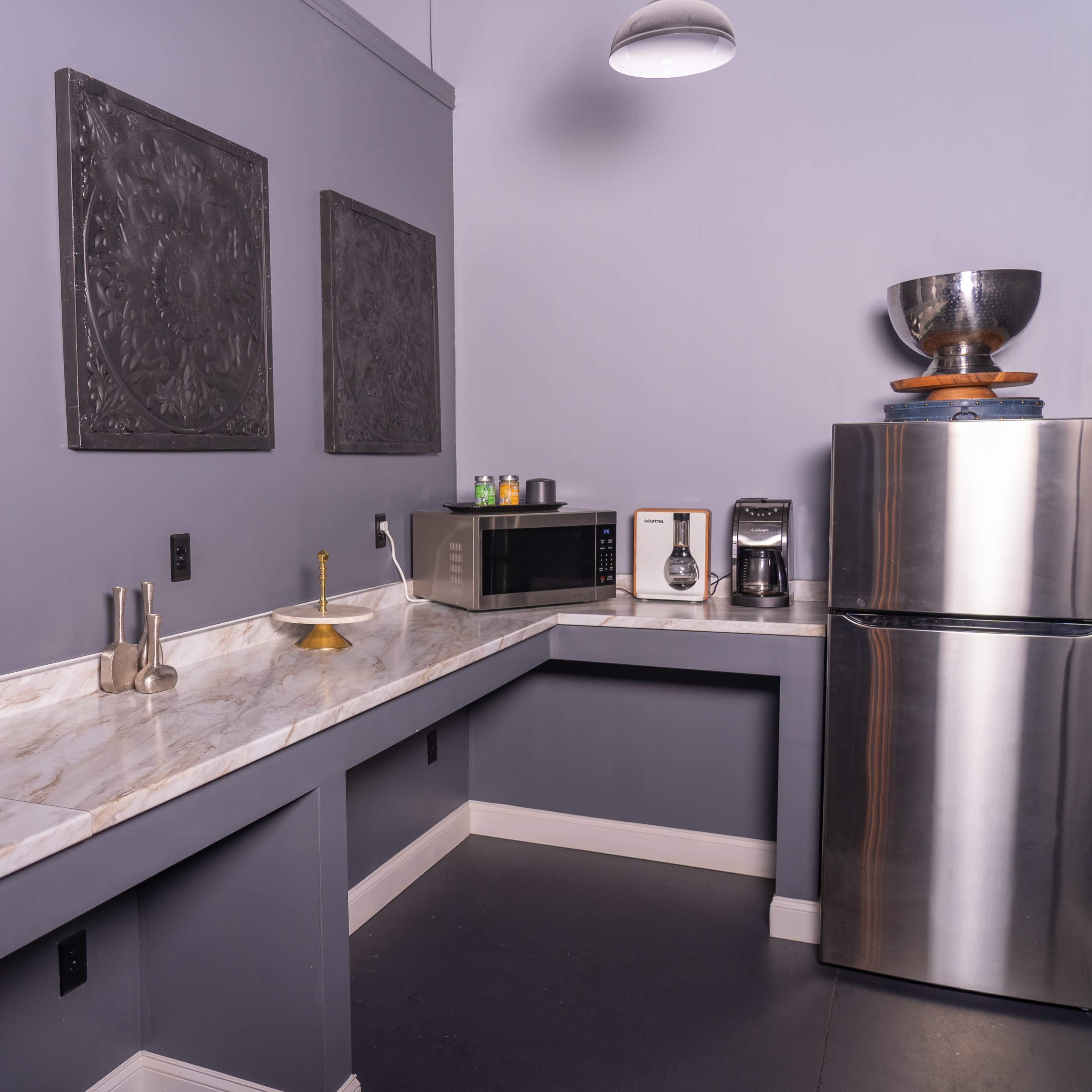 A modern kitchen space with a marble countertop, a stainless steel refrigerator, a microwave, and decorative wall panels.