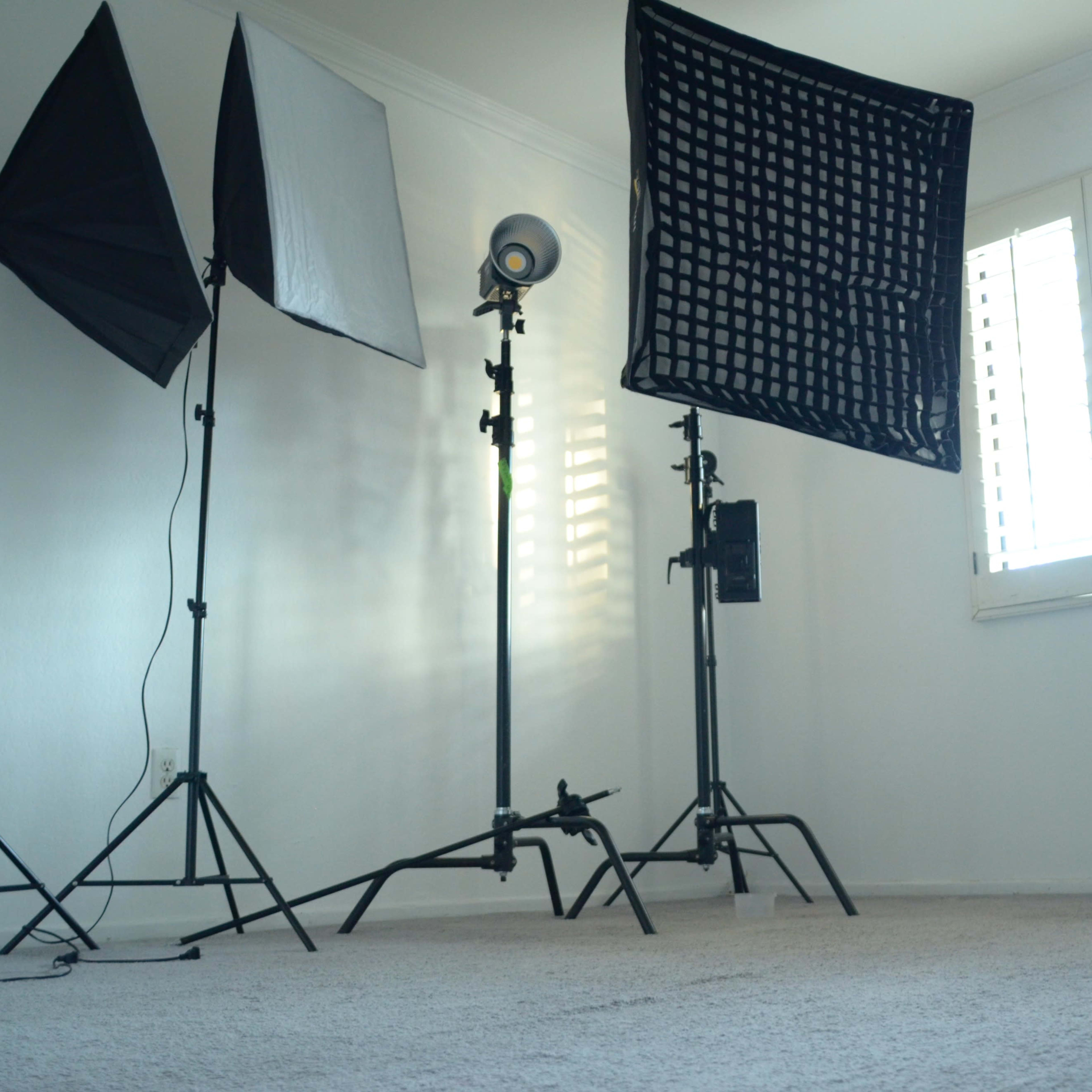 A photography setup with three light stands and softboxes in an empty room with shuttered windows.