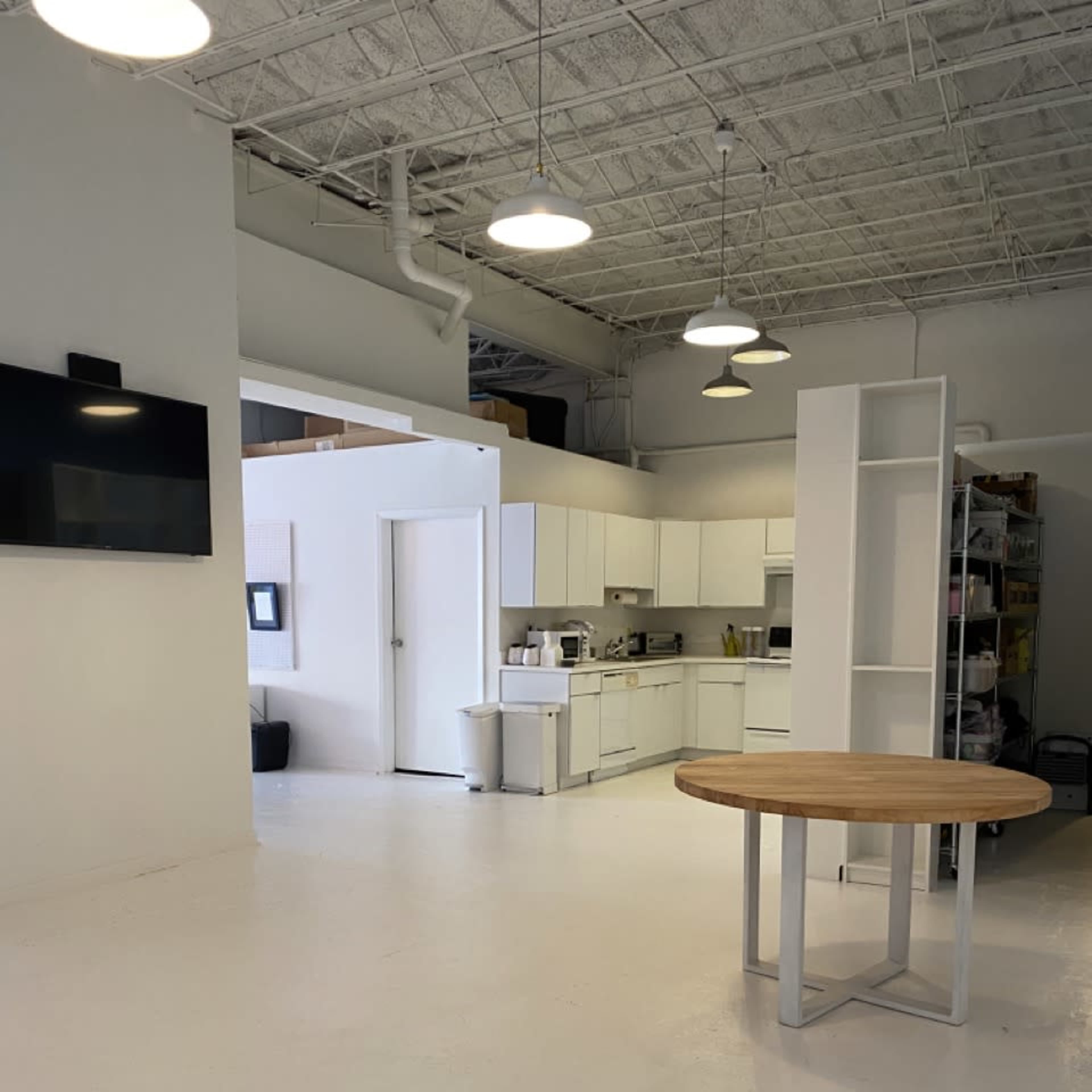 A spacious kitchen area features white cabinetry, a round wooden table, and large lights overhead in a well-lit room.