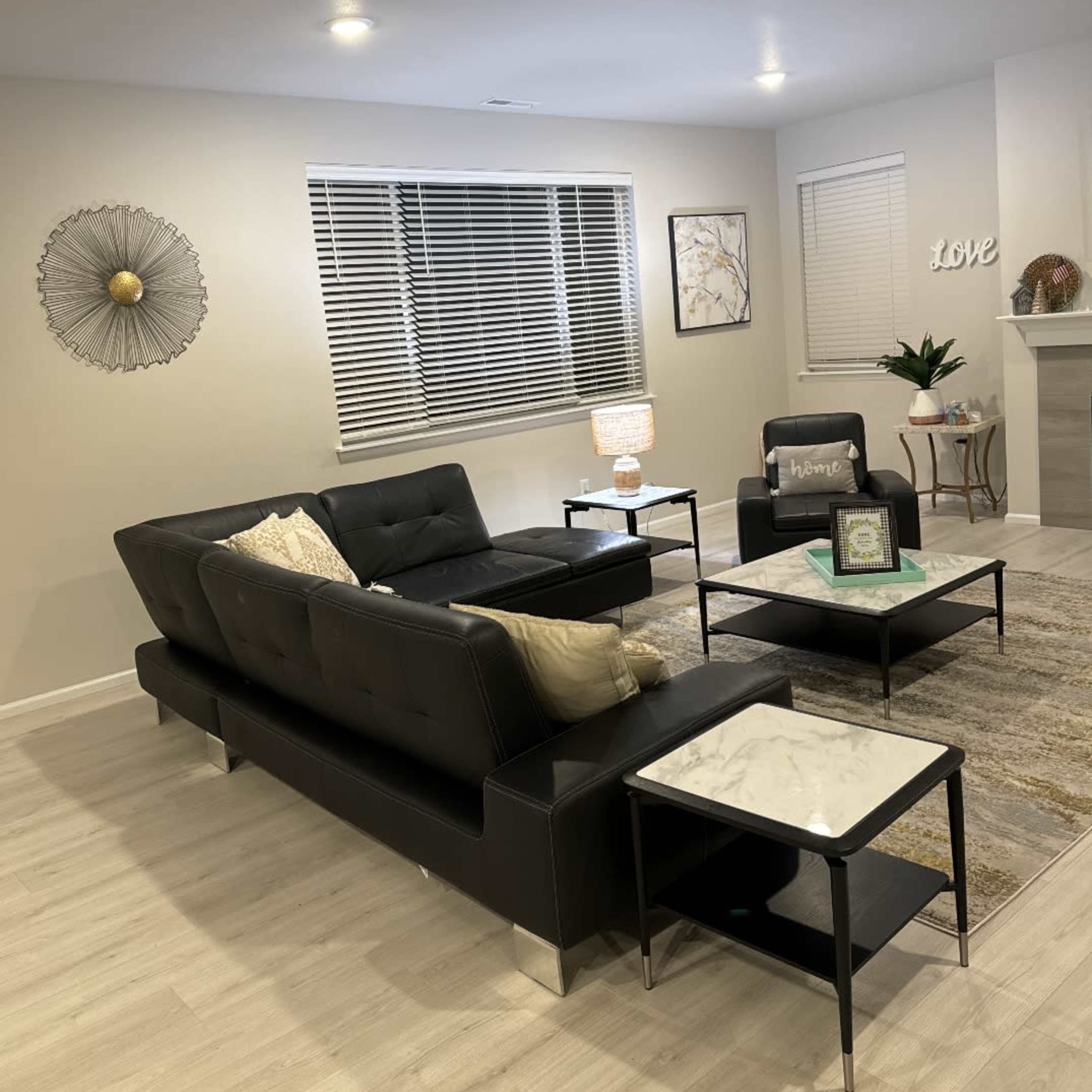 A modern living room features a black leather sofa, two black chairs, and marble-top coffee tables, with decorative wall art and a lamp illuminating the space.