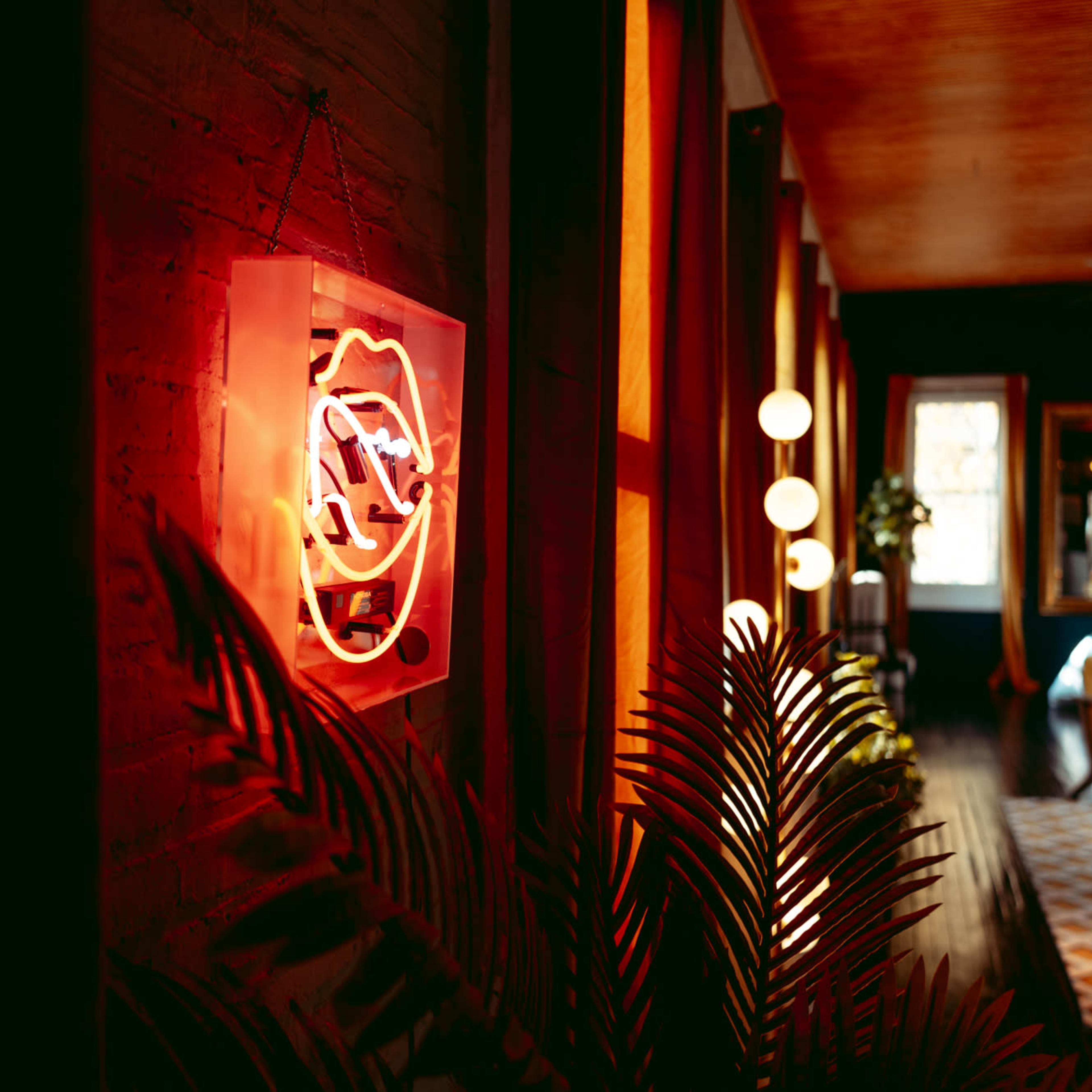A neon sign on a wall illuminated in red, surrounded by wooden flooring and warm lighting in a cozy interior space.