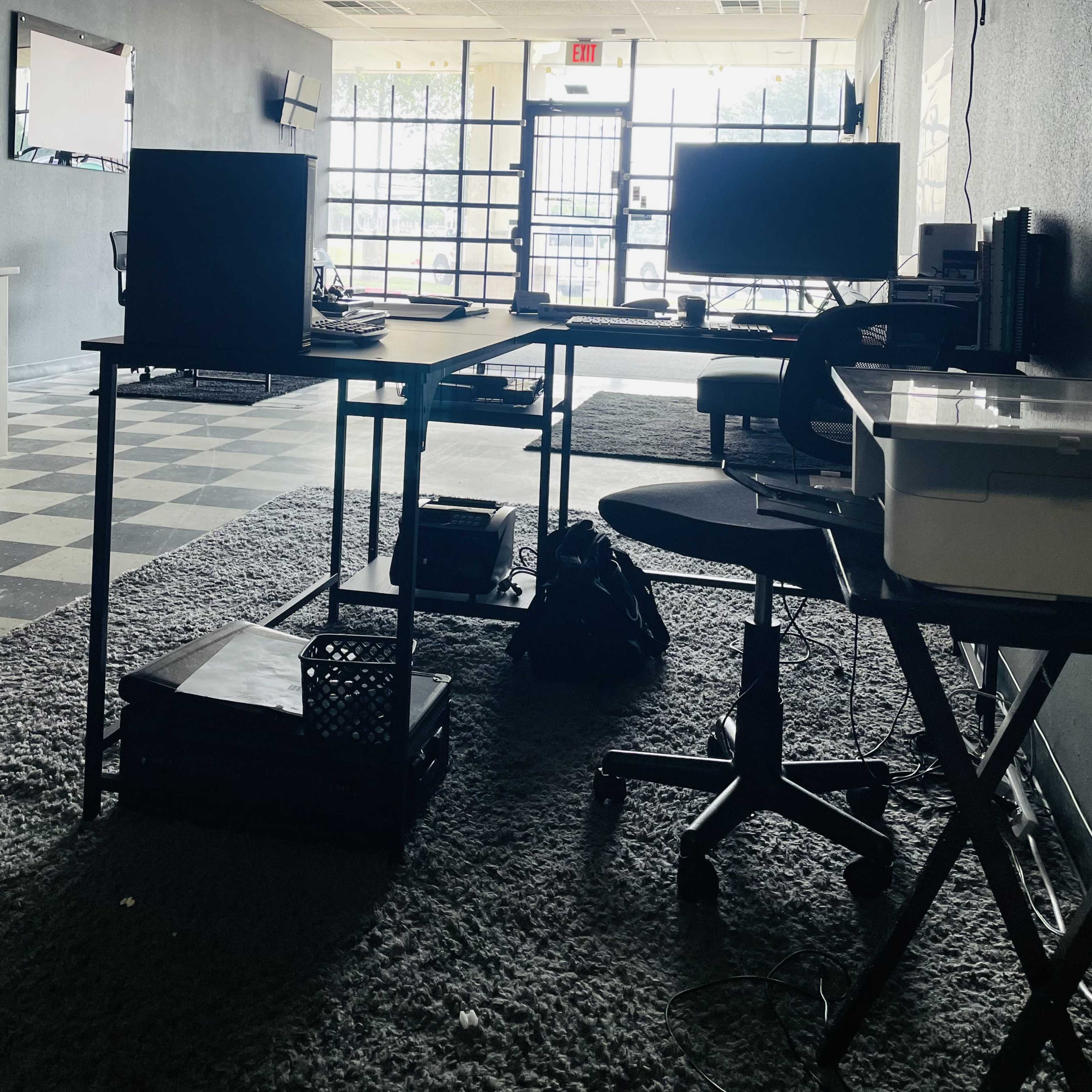An empty office space with black walls, a checkered floor, and two desks positioned near large windows.