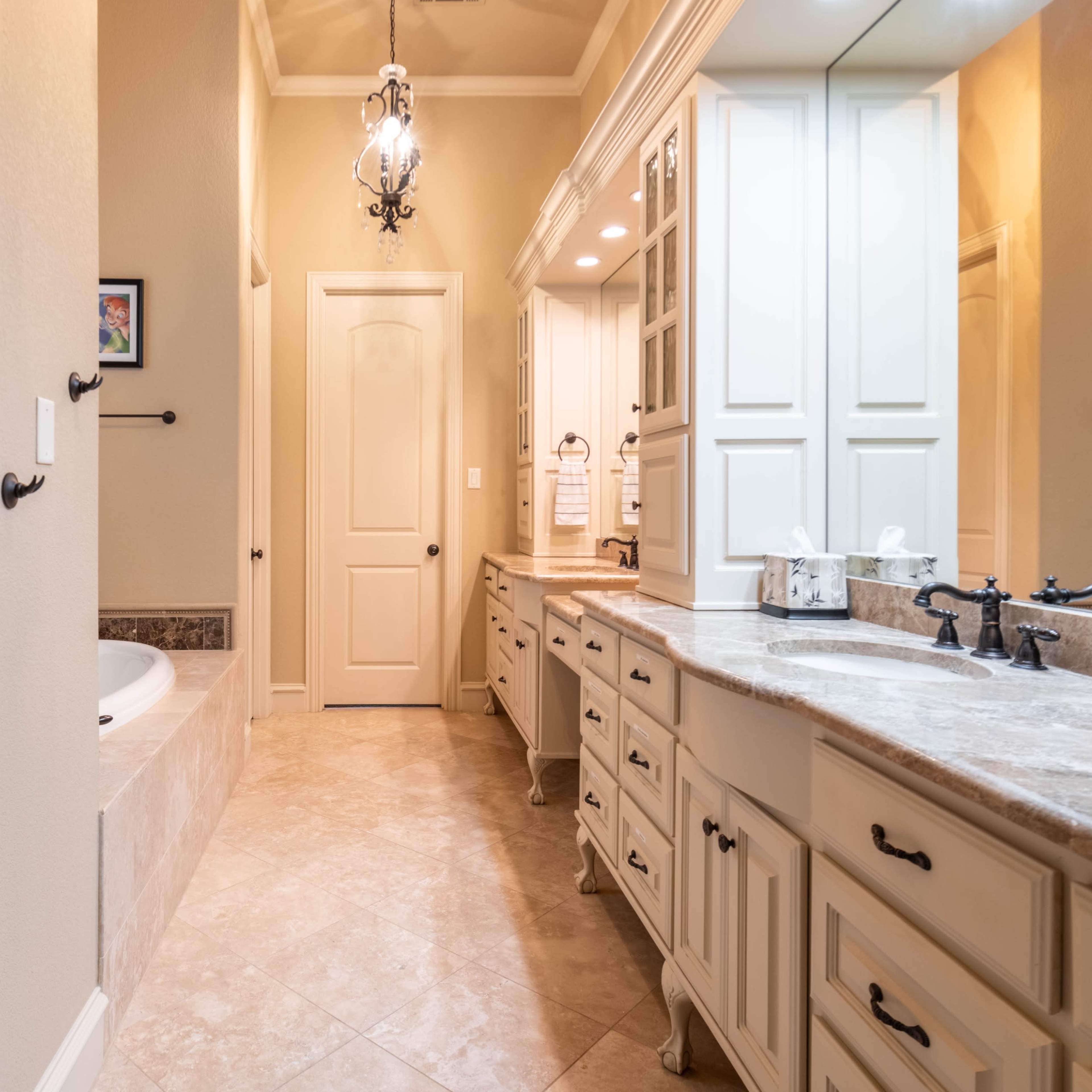 A spacious bathroom featuring a double vanity with white cabinetry, a large bathtub, and a glass-enclosed shower area.