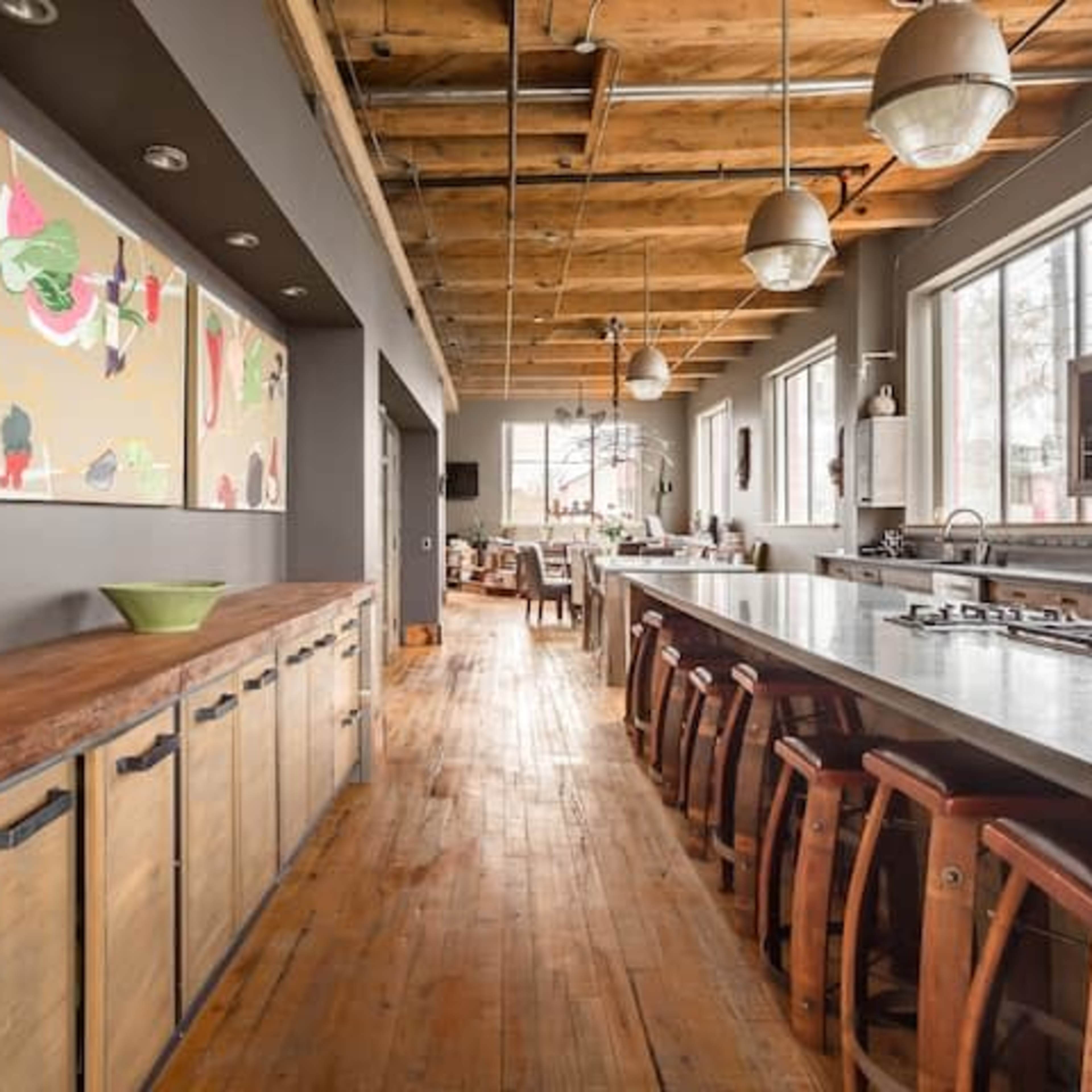 A spacious kitchen with a long countertop, wooden stools, and colorful artwork on the walls.