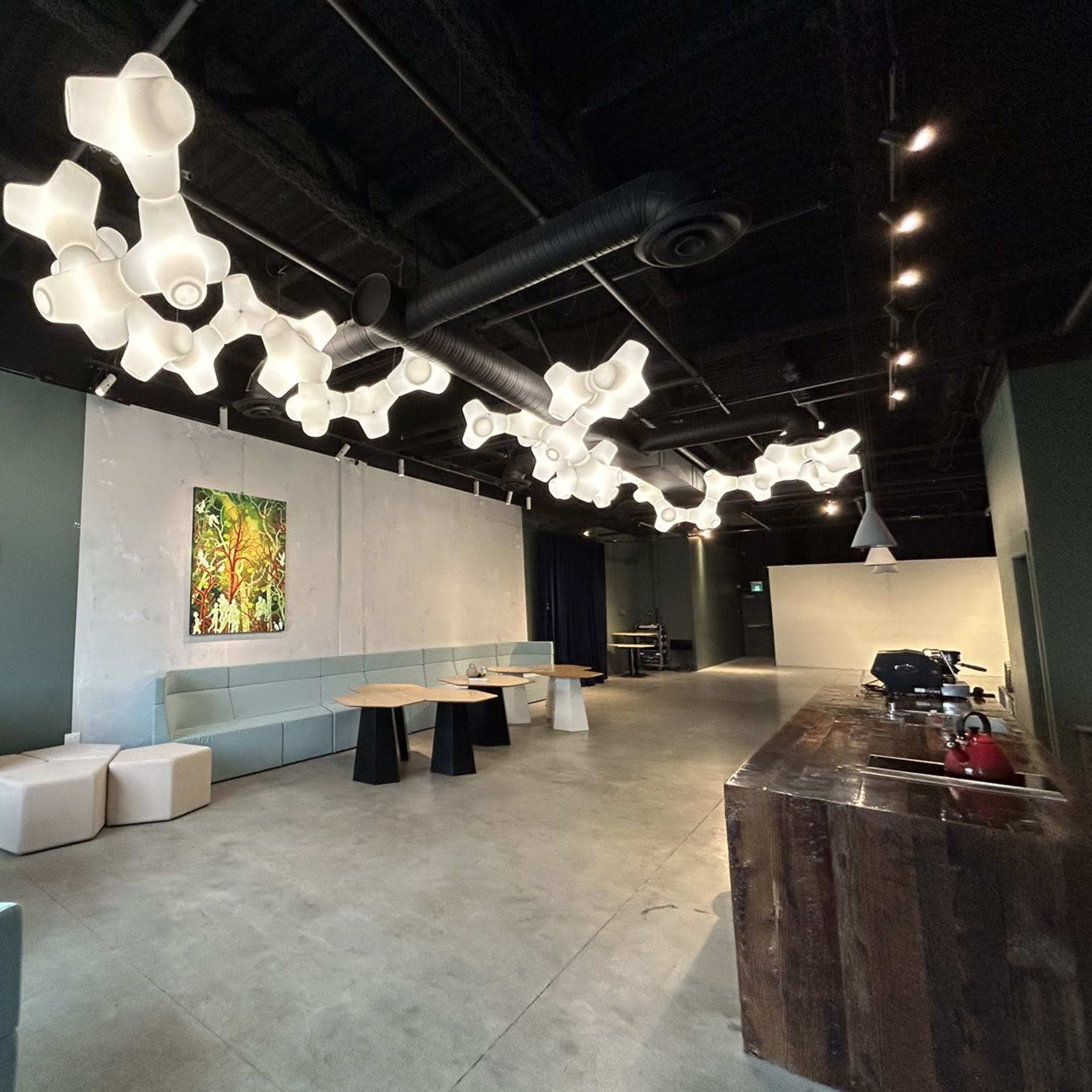 A spacious cafe interior featuring unique ceiling lights, modern seating arrangements, and artworks on the walls.