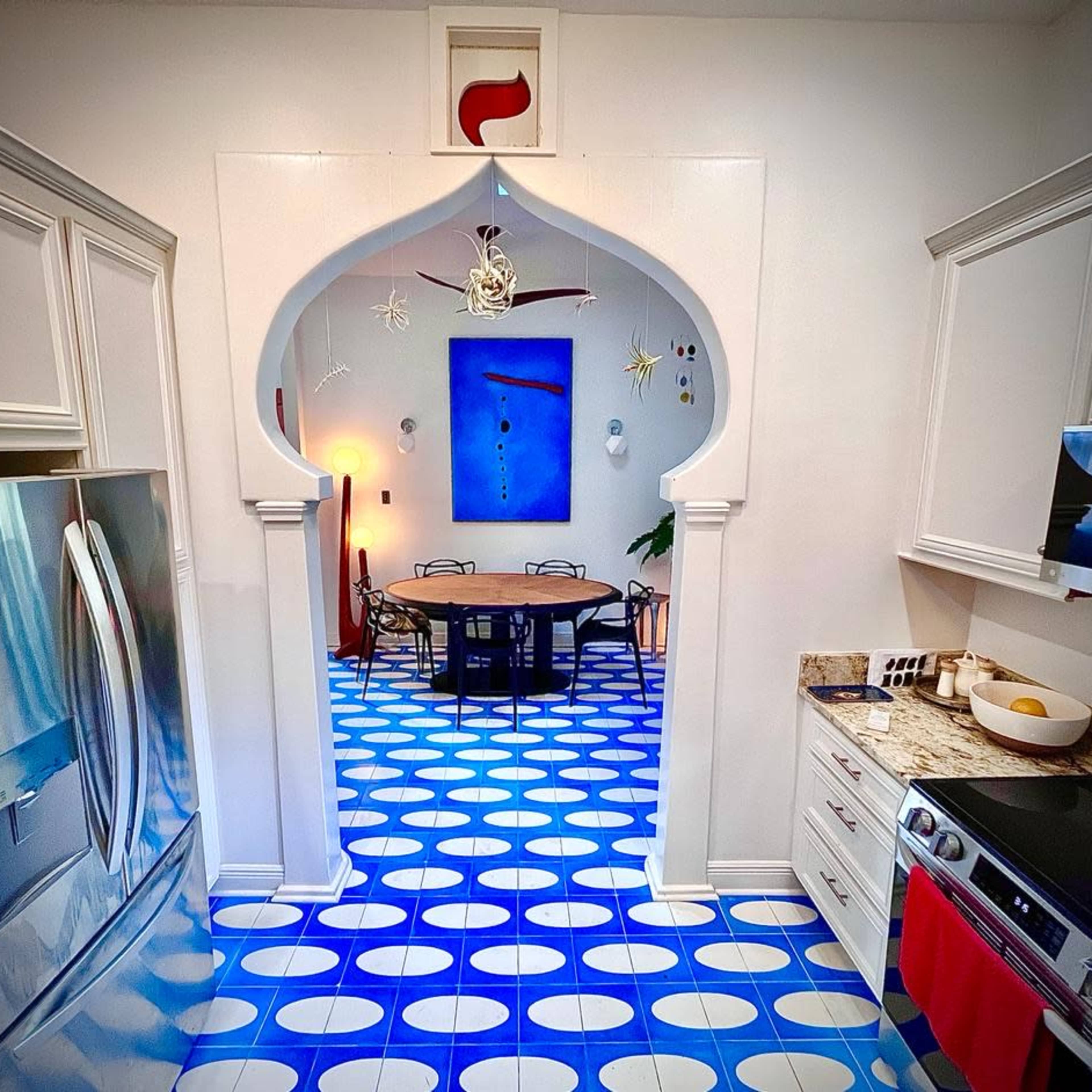 A kitchen features a rounded archway leading to a dining area with a blue circular tiled floor and minimalist decor.