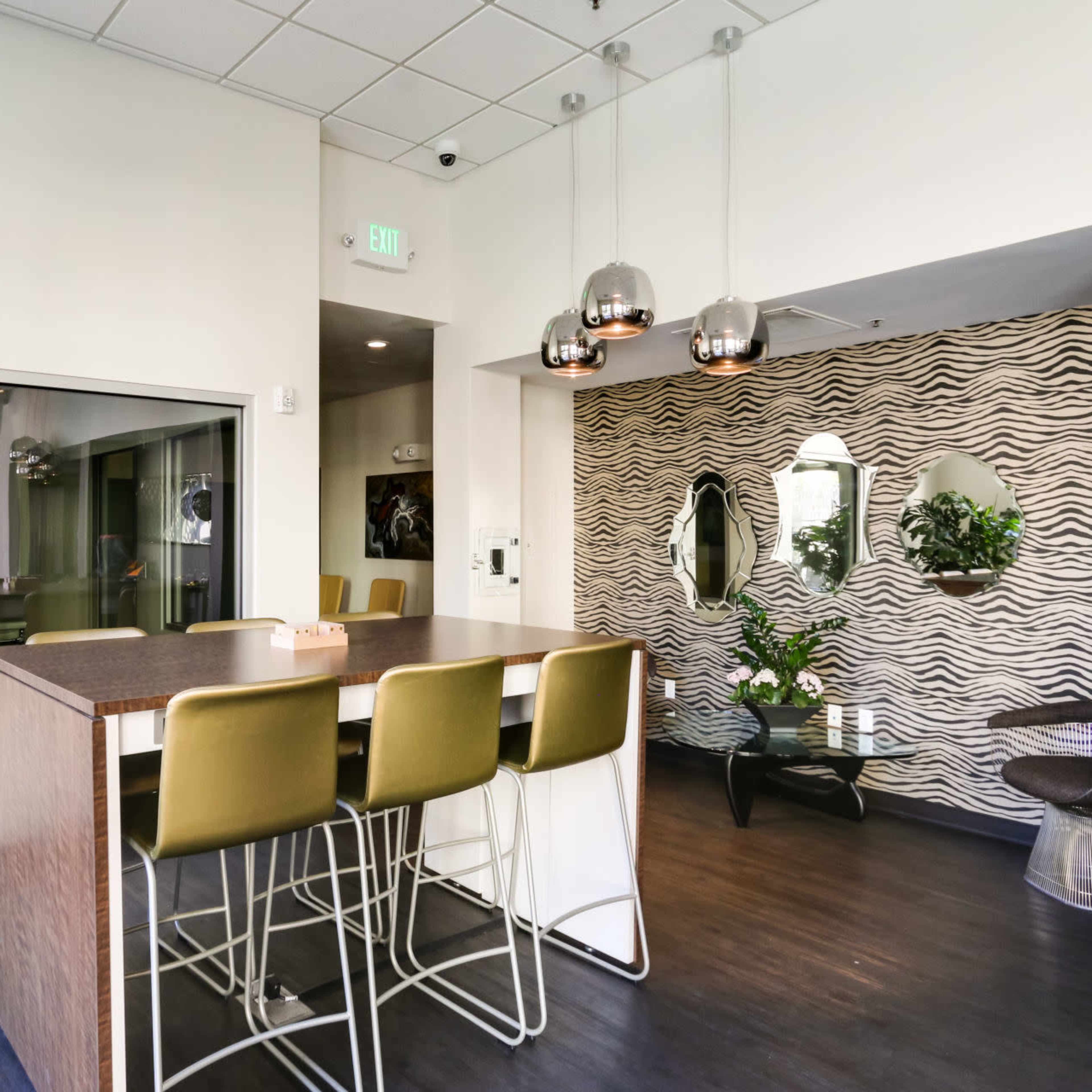 A modern interior space featuring a bar-height table with four green stools, a large indoor plant, and a decorative wall with mirrors and plants.