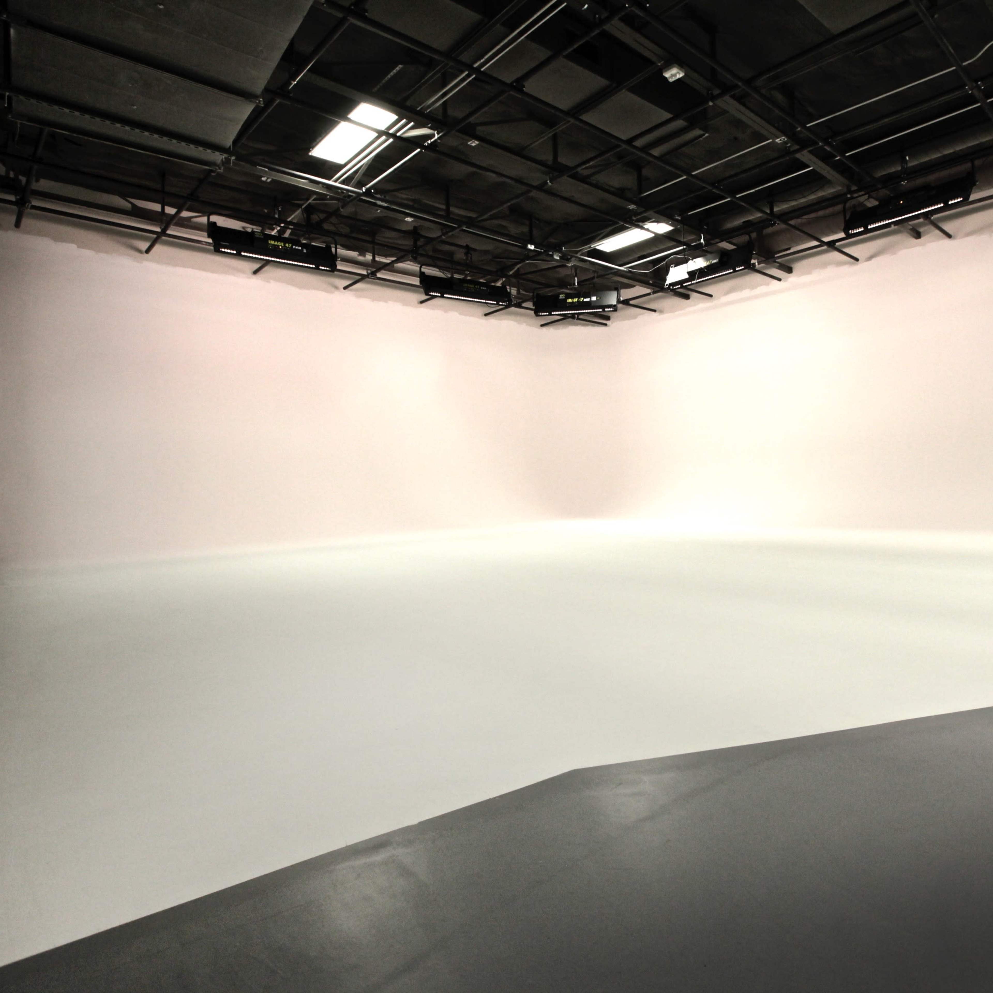 A large, empty studio space with a seamless white backdrop and a smooth floor.