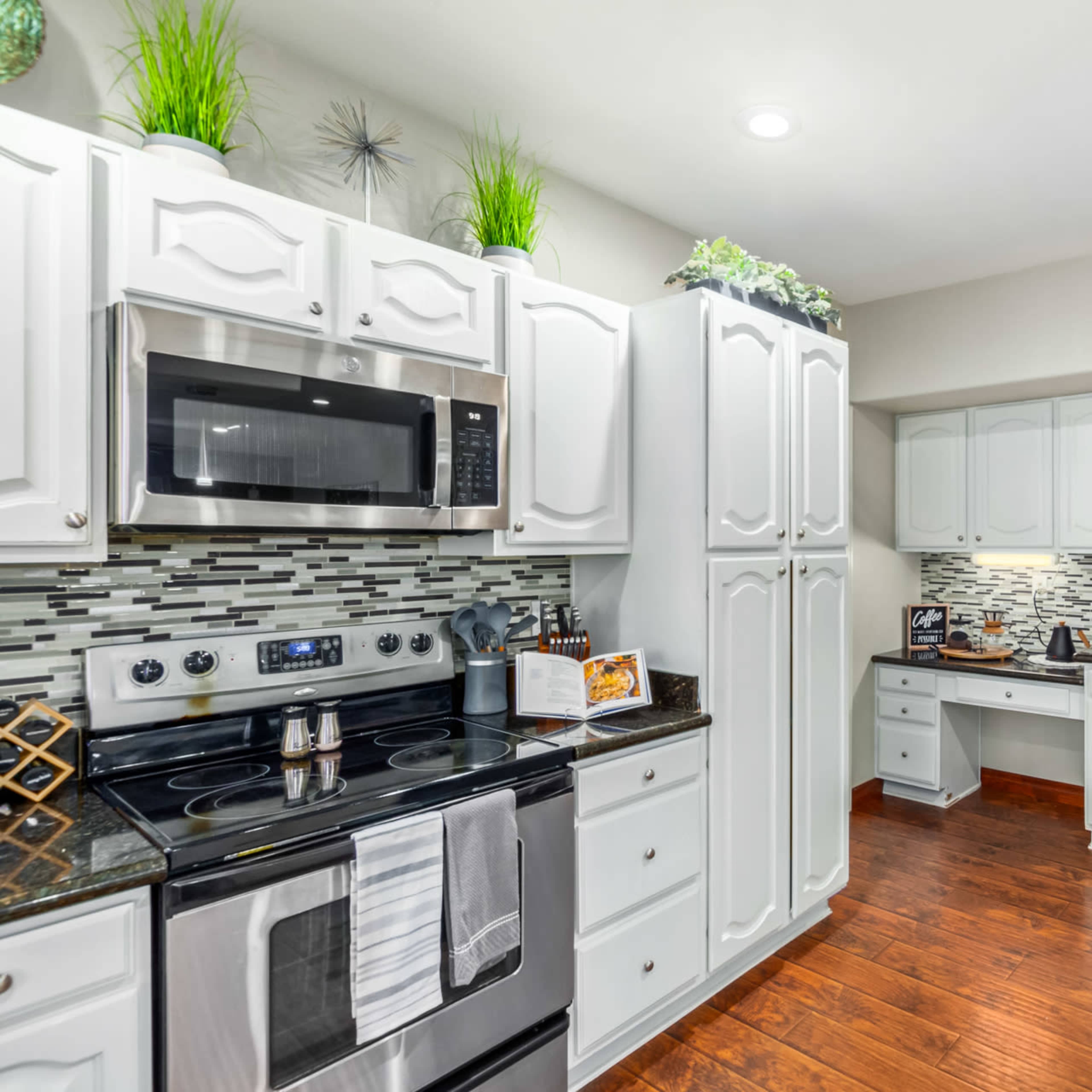 A modern kitchen features white cabinetry, a stainless steel refrigerator, and dark countertops with a glass tile backsplash.