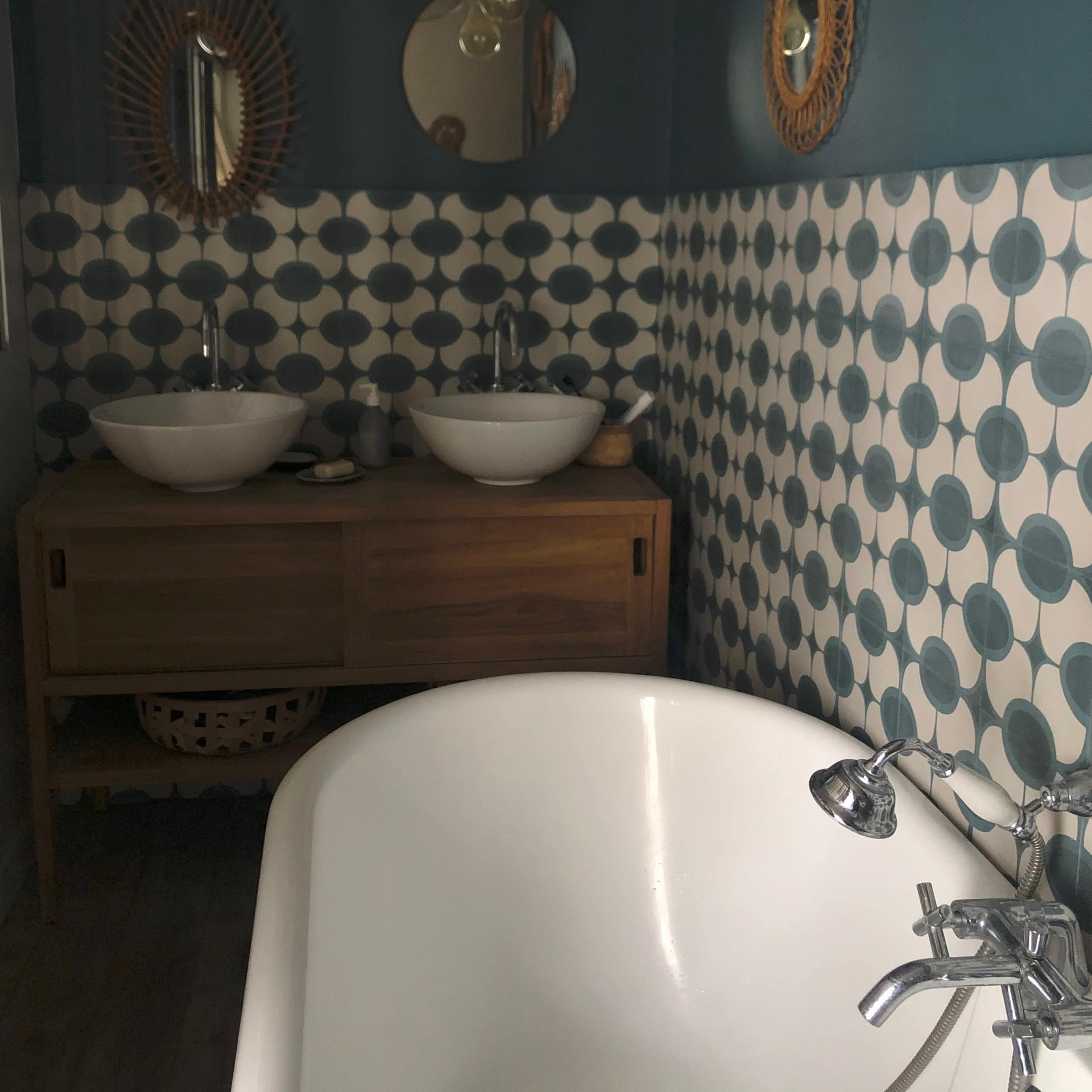 A bathroom featuring a freestanding white bathtub, two circular sinks on a wooden vanity, and walls decorated with circular patterned tiles.