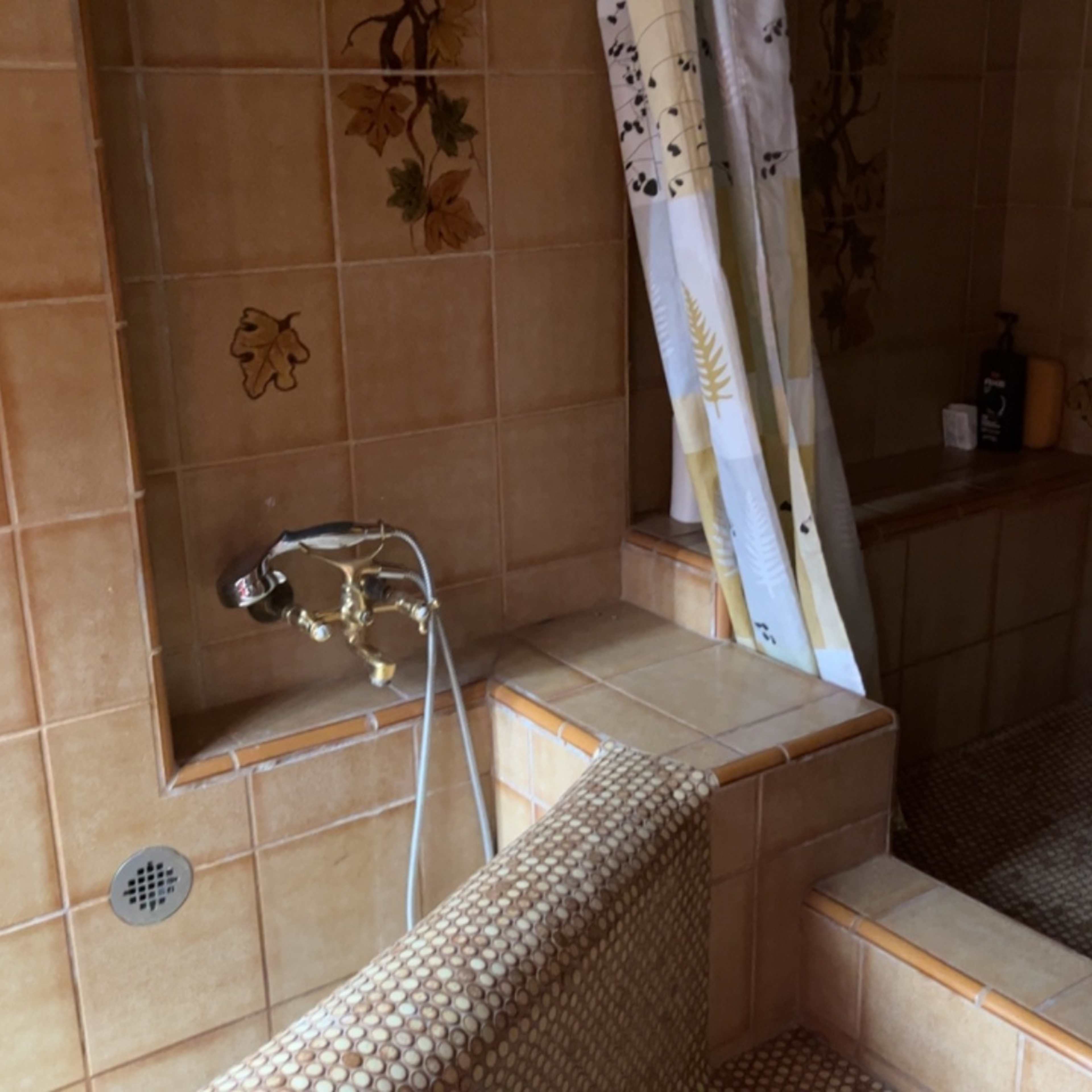 A tiled bathroom featuring a shower area with a curtain, a faucet, and a built-in bench.
