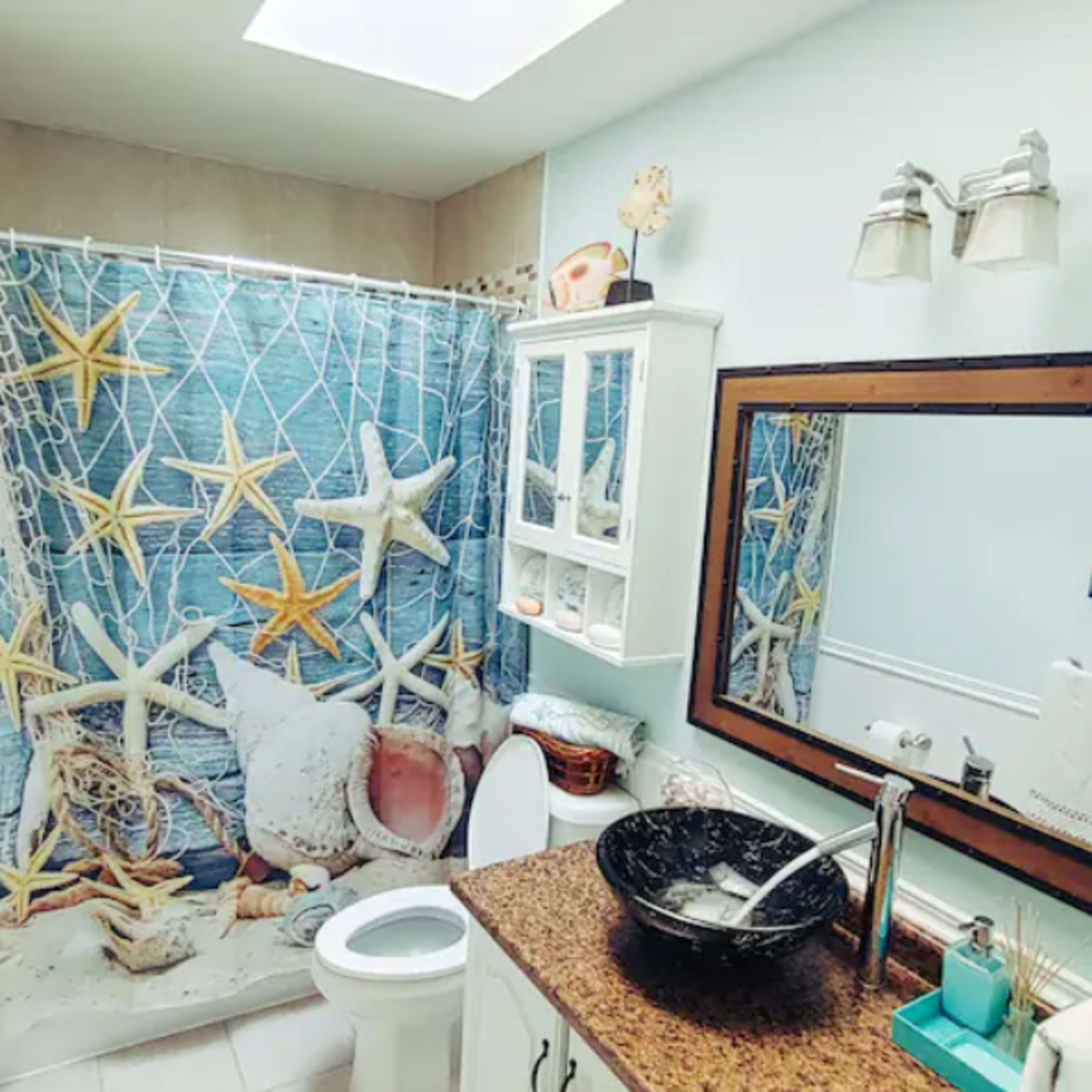 A bathroom with a blue and white starfish-themed shower curtain, a granite countertop sink, and a large mirror above it.