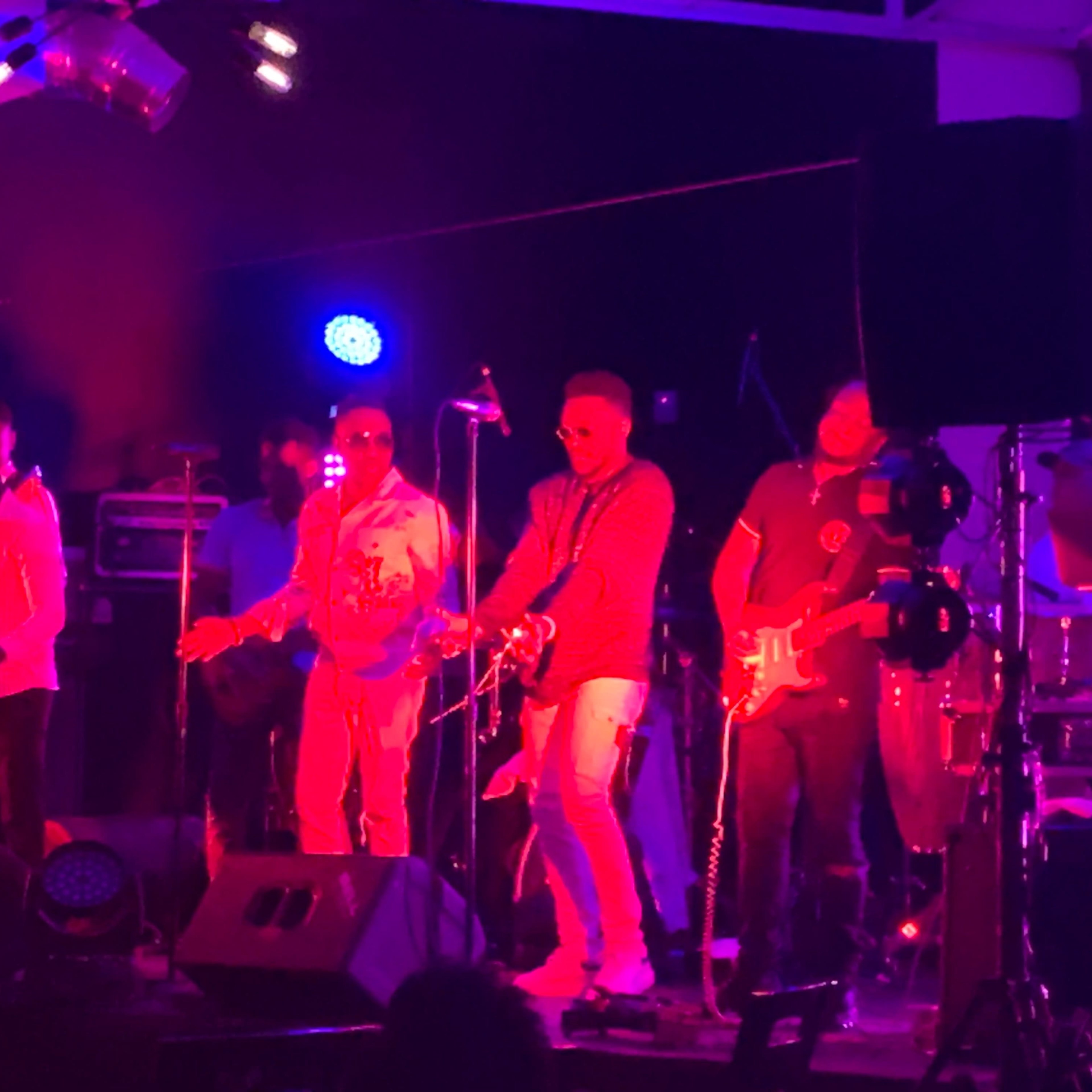 A band performs on stage with colorful lighting and various instruments, including a keyboard and guitars.