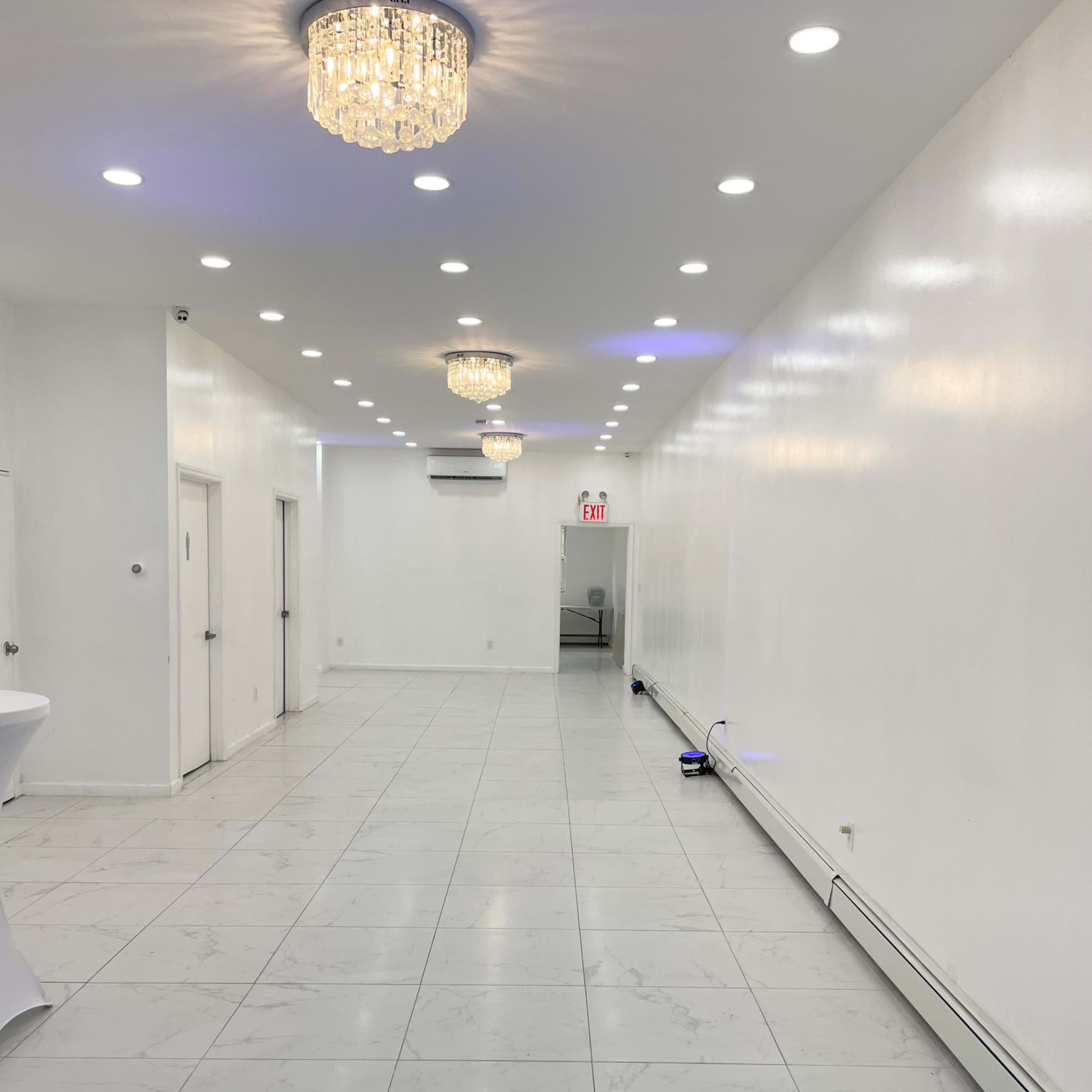 A long, brightly lit corridor with white walls and multiple chandeliers hanging from the ceiling.