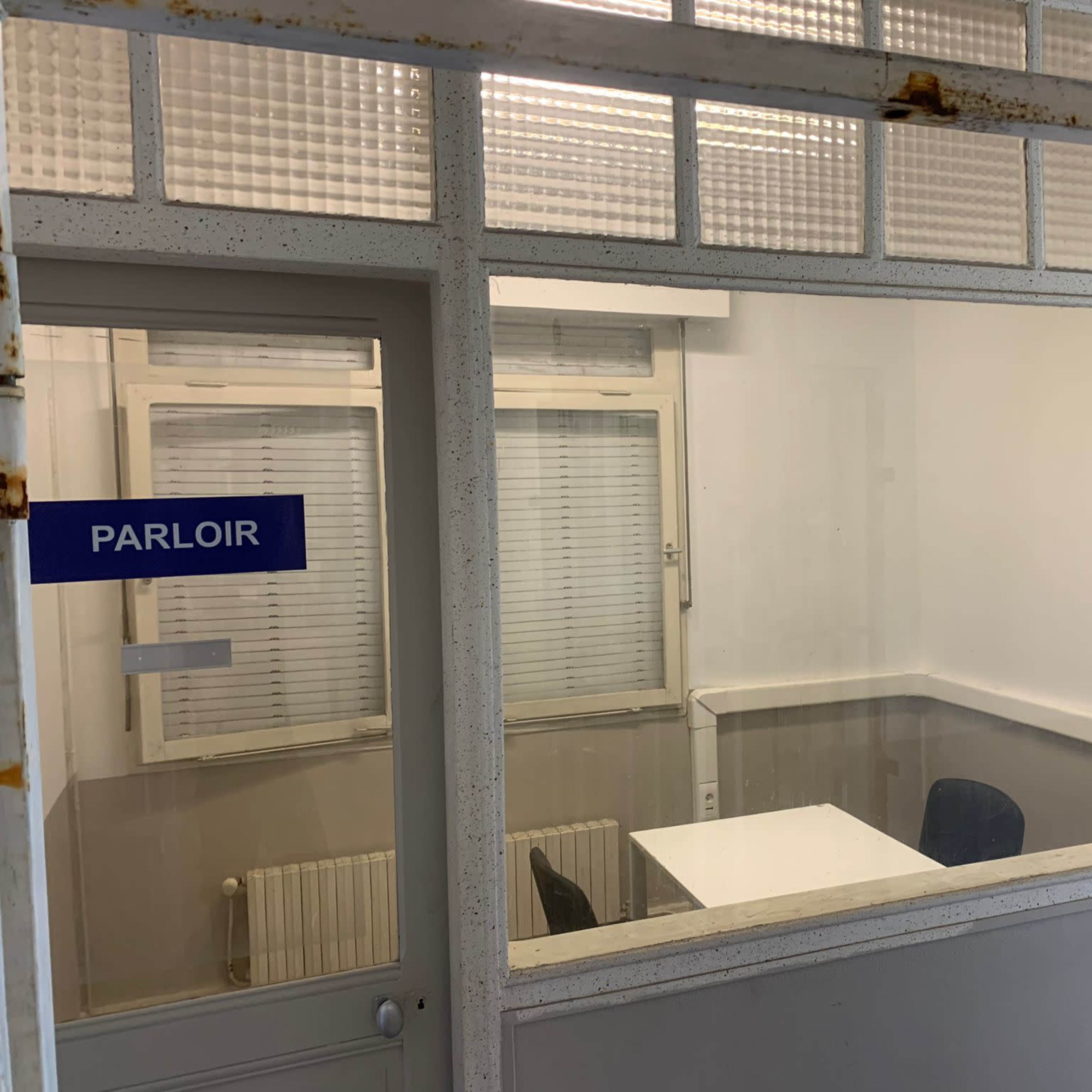 A small office with a white table and two chairs, visible through glass walls, labeled as "PARLOIR."