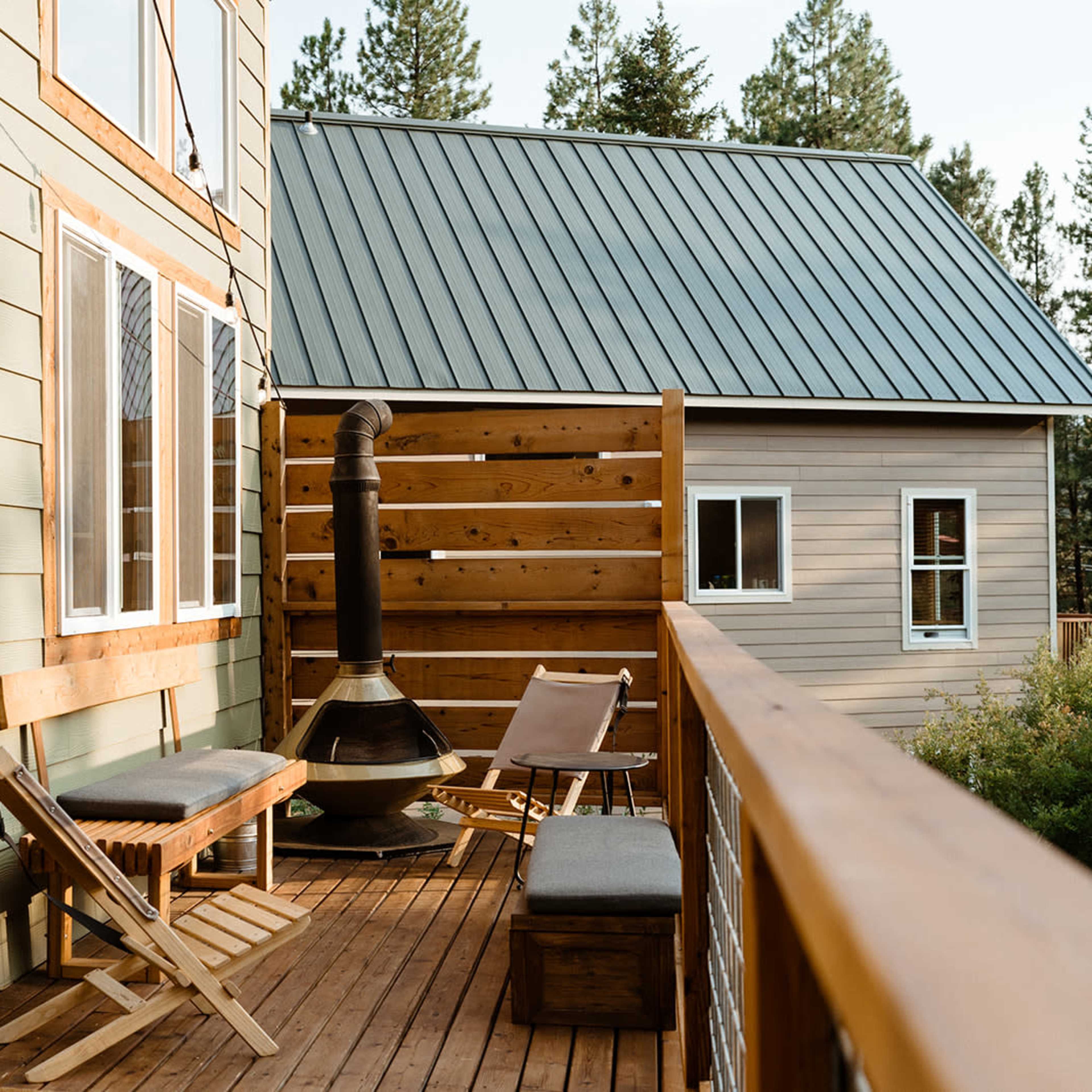 A wooden deck with two seating areas, a modern fireplace, and a view of nearby houses under a clear sky.
