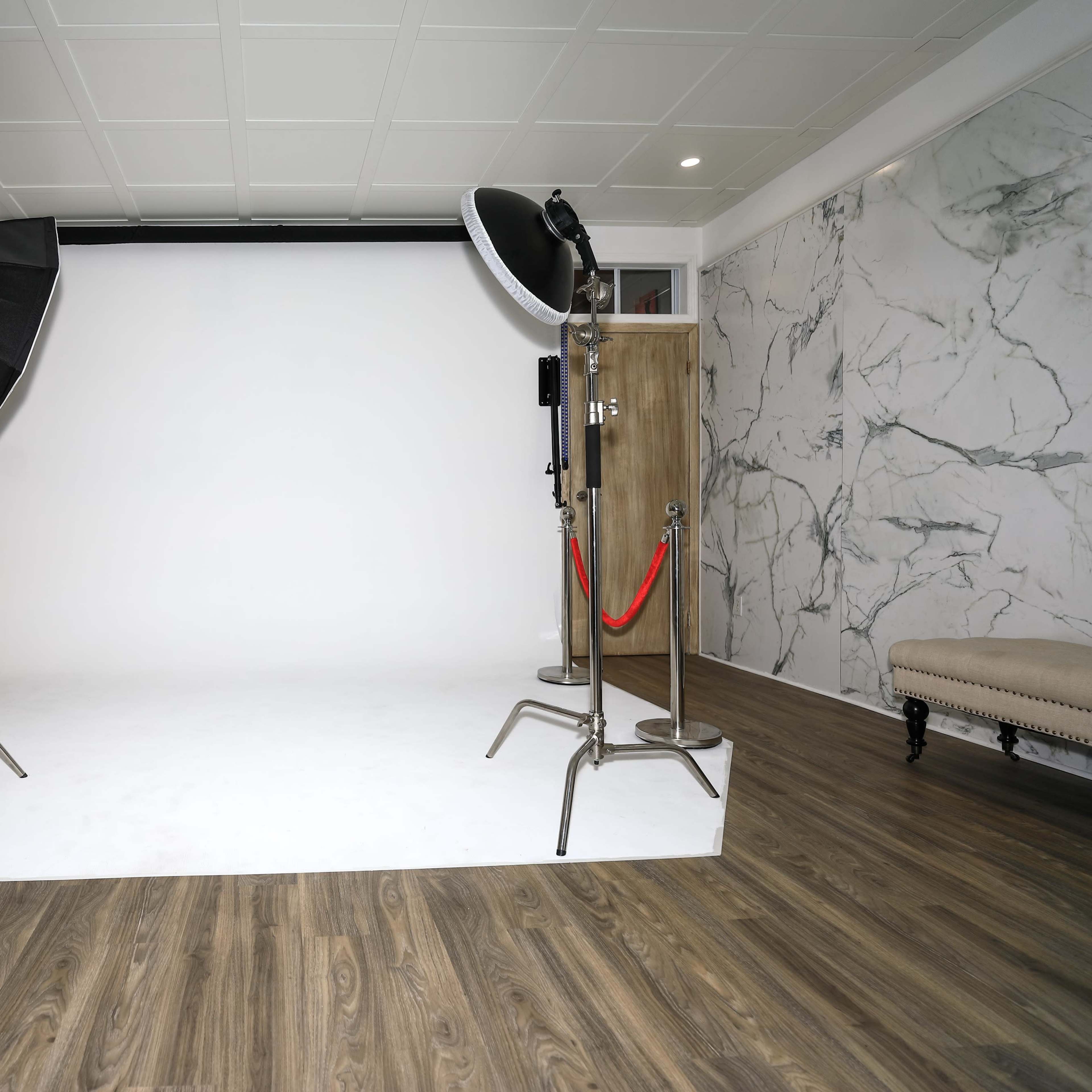 A photography studio with a plain white backdrop, two softbox lights, and hardwood flooring.