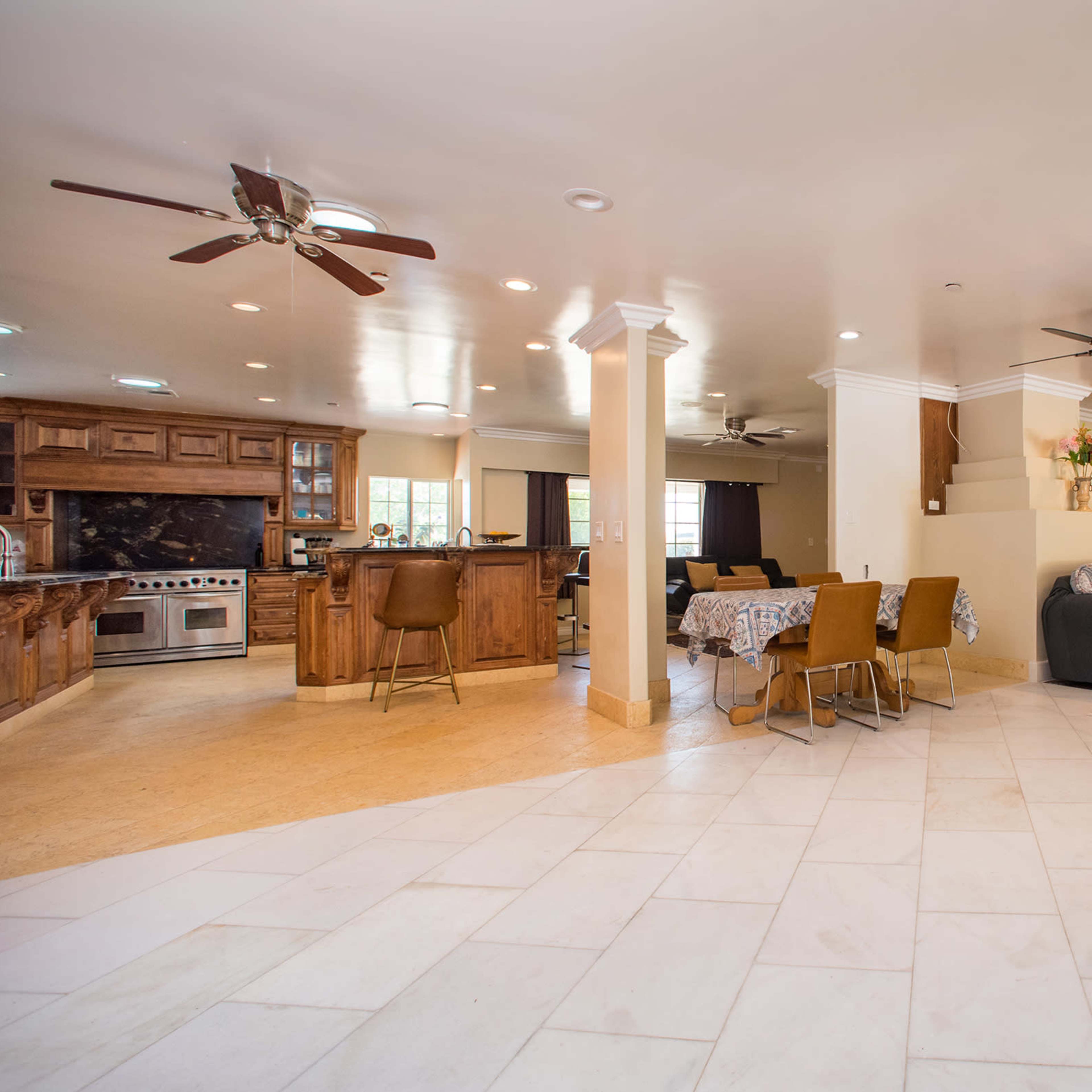 A spacious living area with tiled flooring, a kitchen in the background, and a seating area featuring a sofa and dining table.