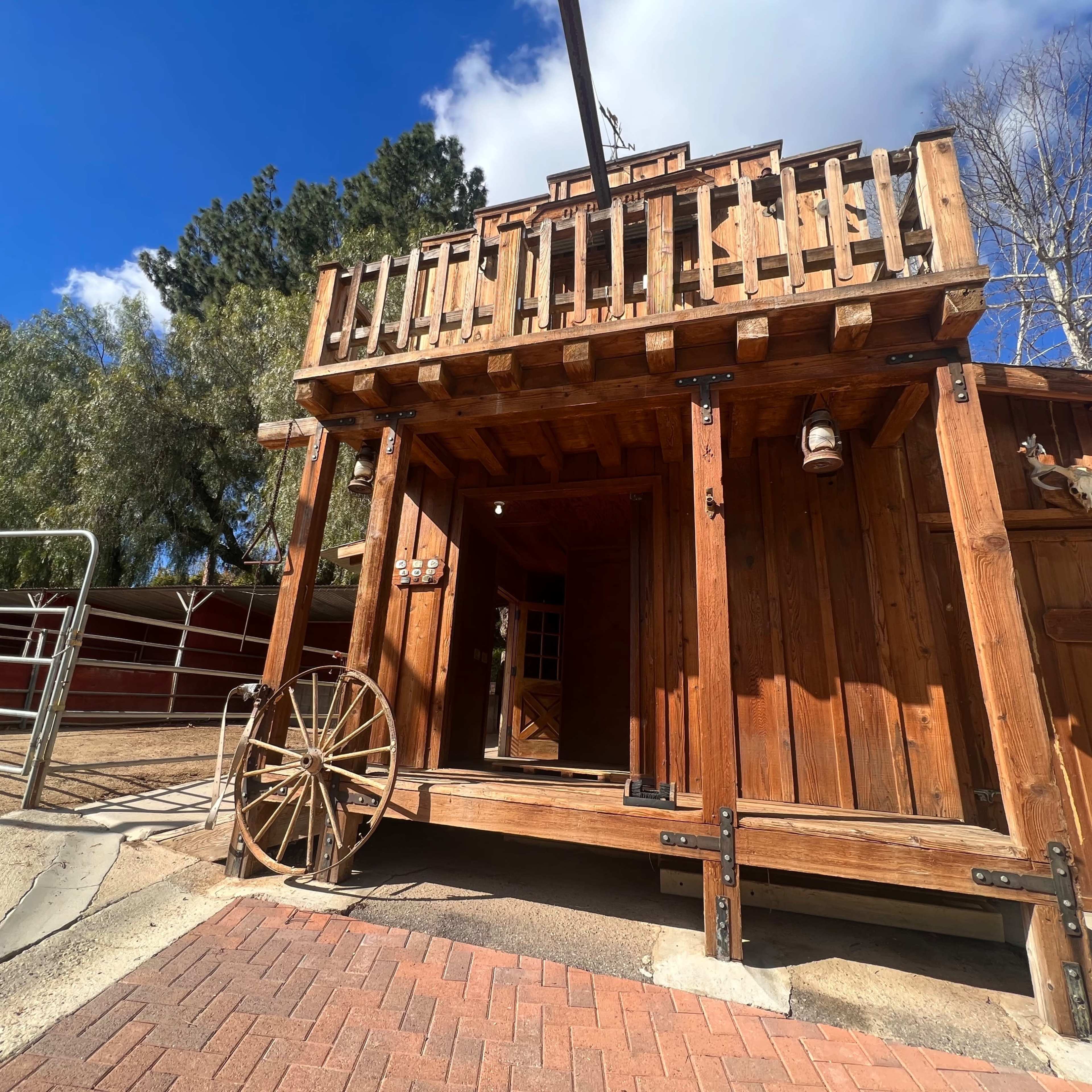 A wooden structure features a porch with railings and a wagon wheel beside the entrance.