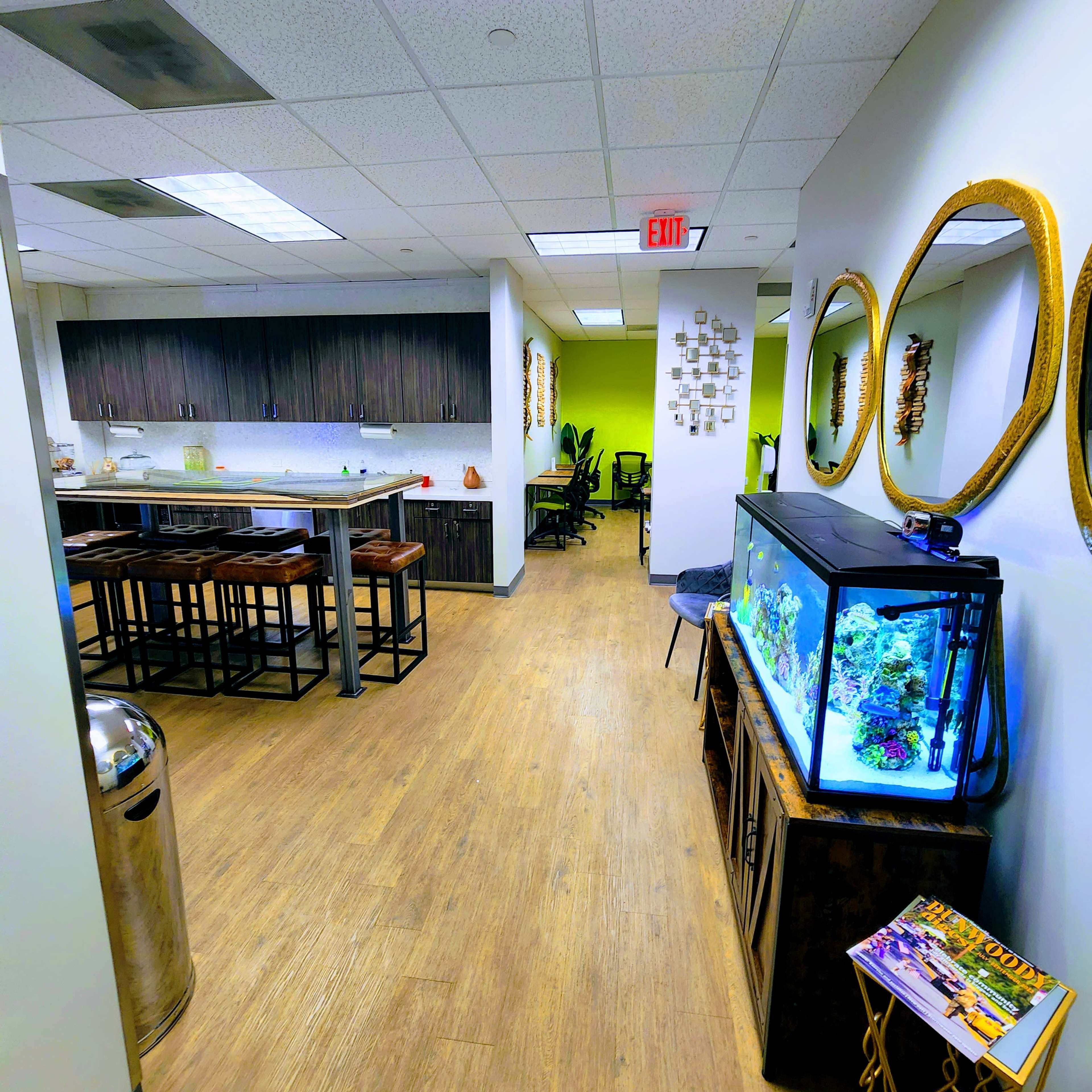 A modern office space features a kitchen area with bar seating, an aquarium, and decorative mirrors along the walls.