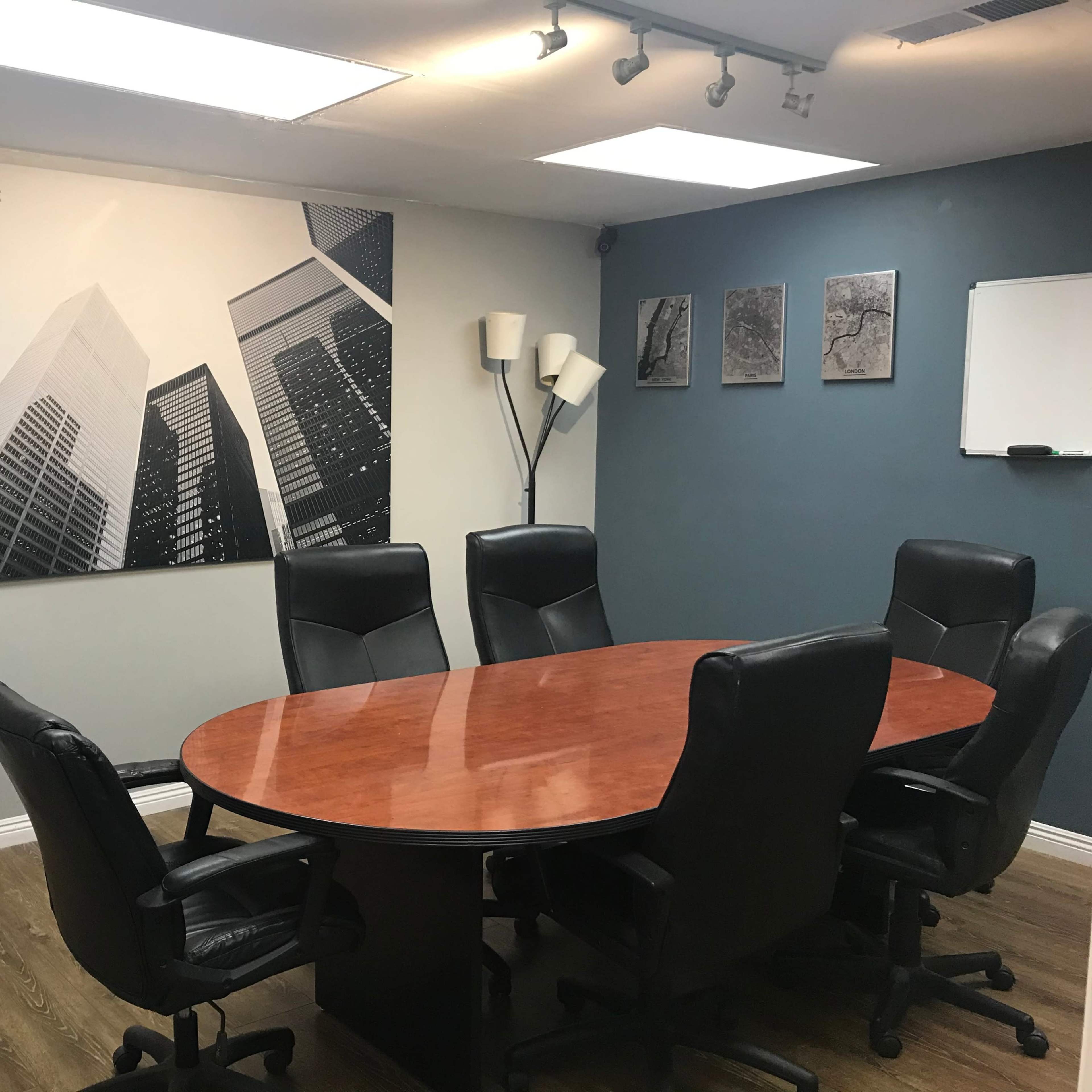 A conference room features a large wooden table surrounded by black ergonomic chairs, with a large black-and-white cityscape photograph on the wall.