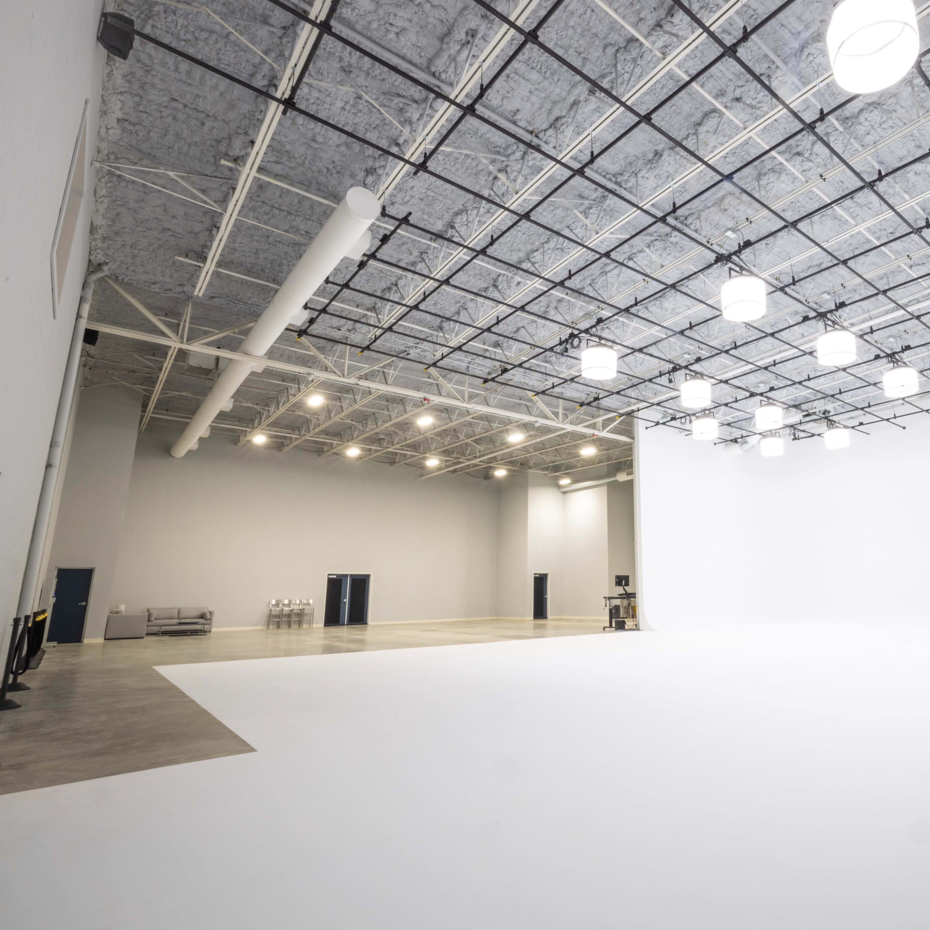 A large, empty studio space with a white wall and a ceiling grid of lights.