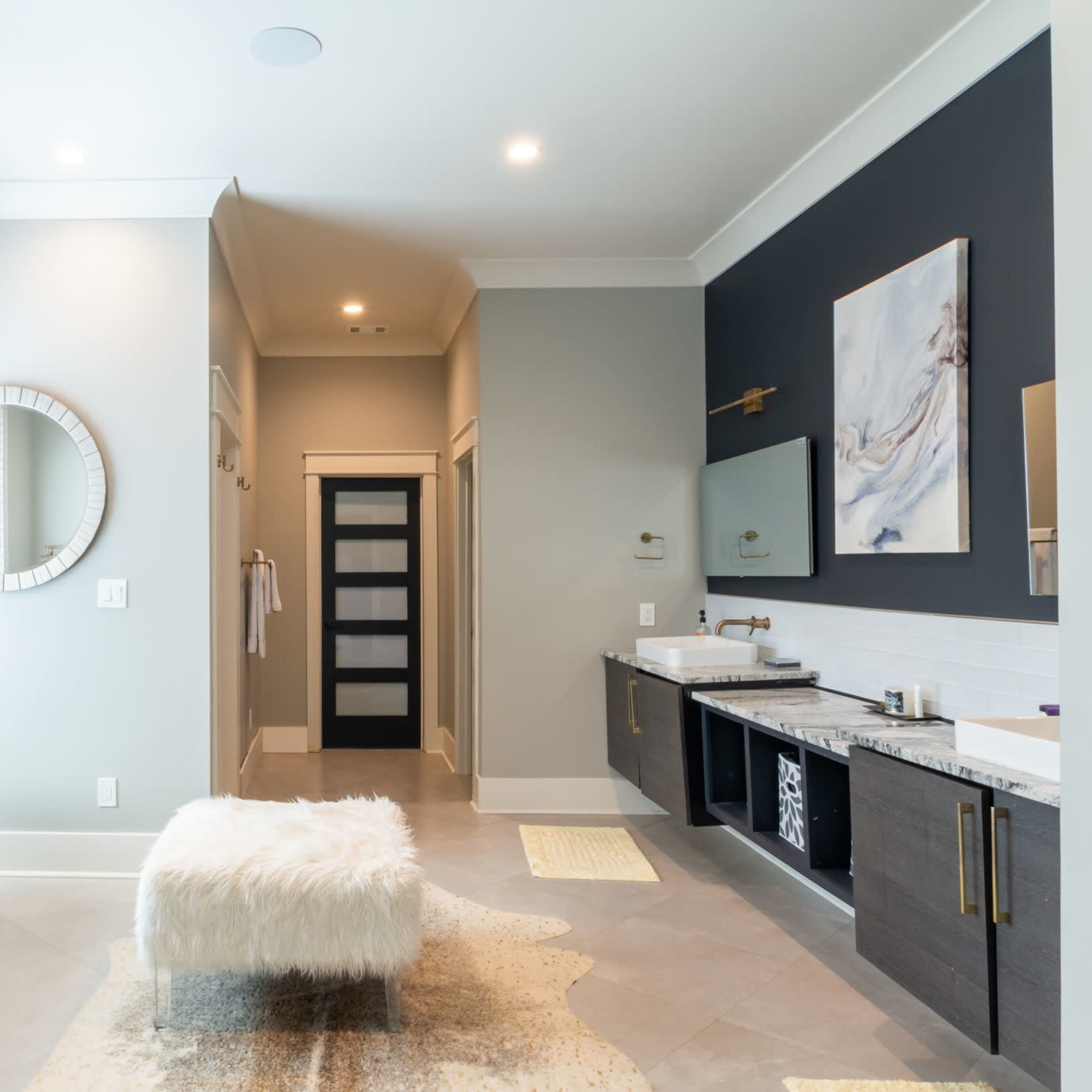 A modern bathroom featuring a freestanding black bathtub, a round mirror, and a double vanity with a dark cabinetry and light countertops.
