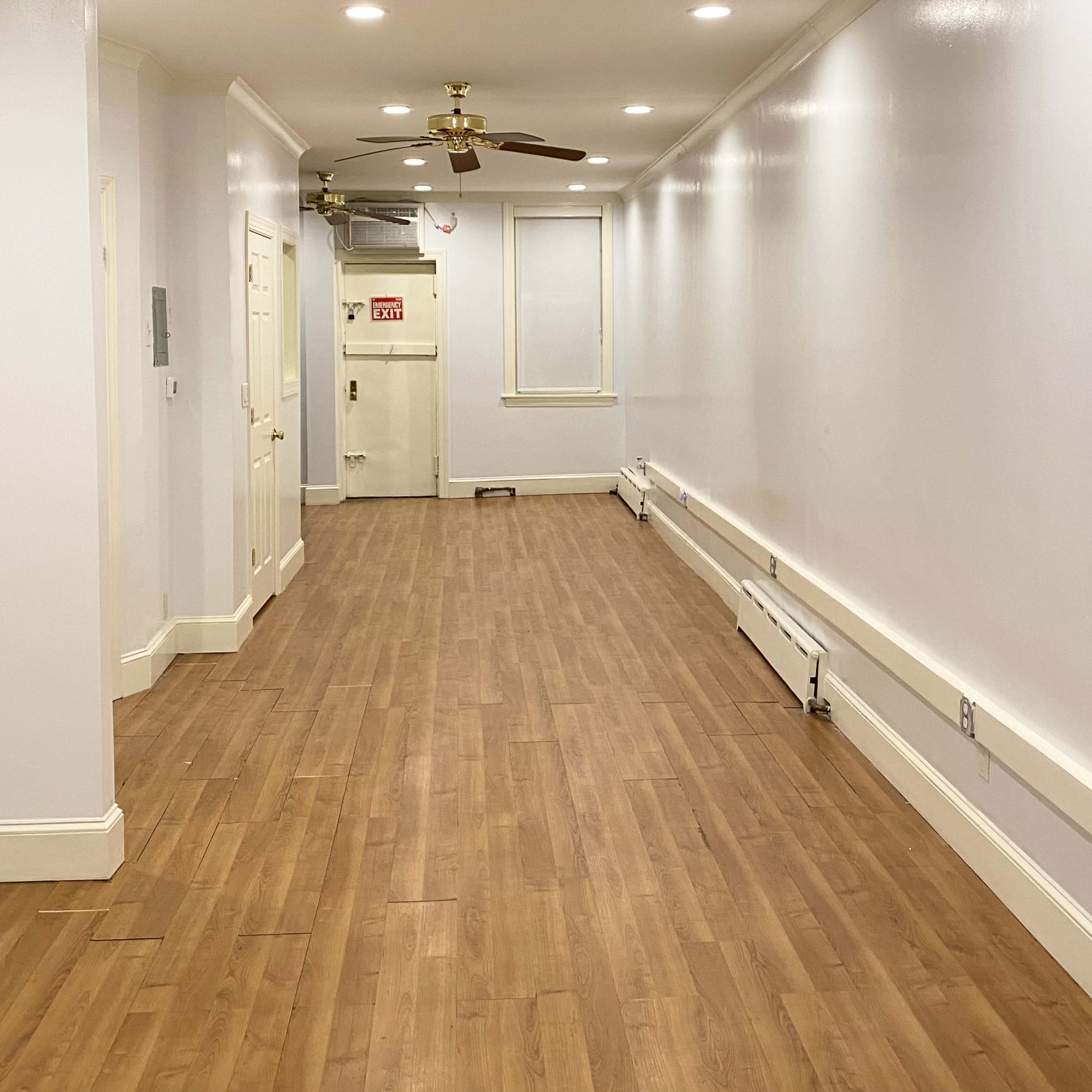 A long, narrow hallway with wood flooring, white walls, and a ceiling fan.