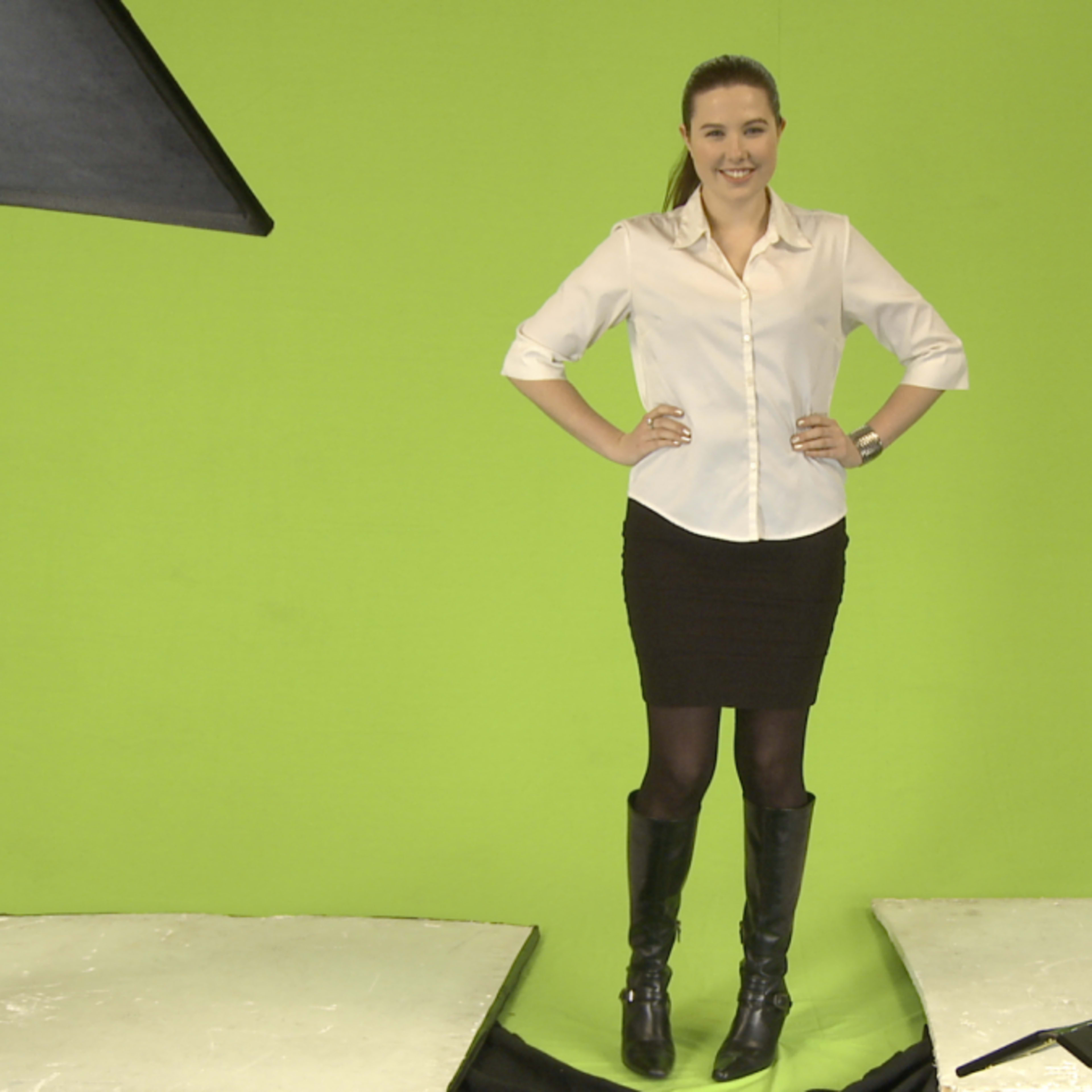A woman in a white blouse and a black skirt stands confidently on a stage with a green screen backdrop.